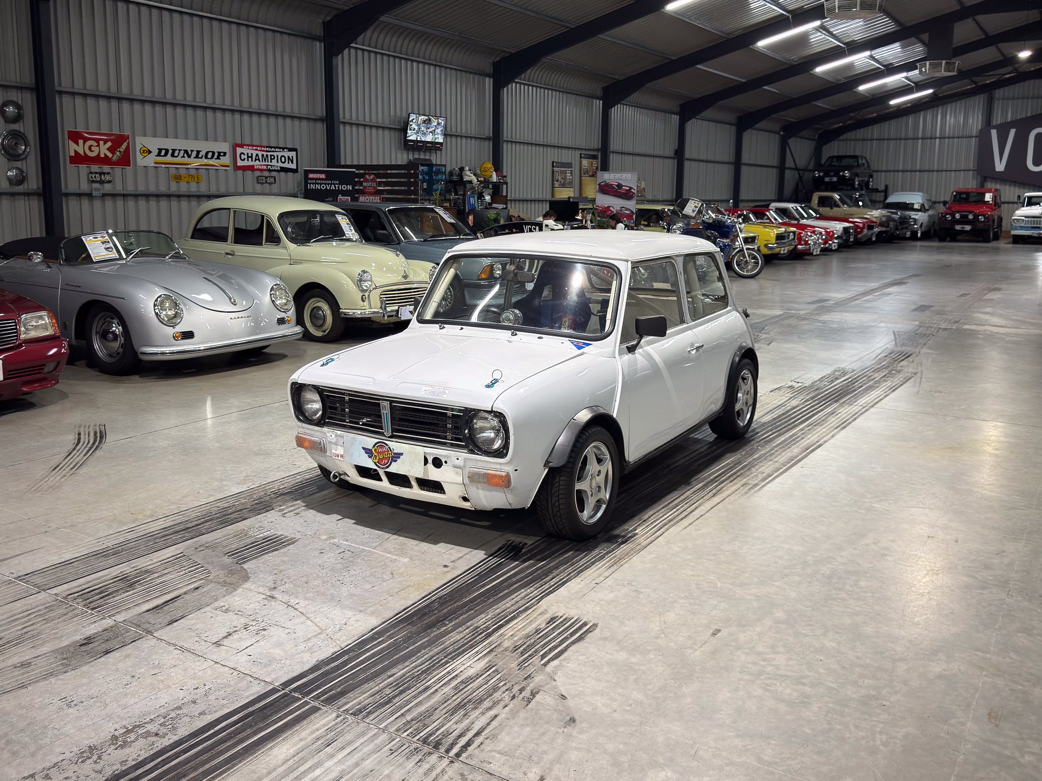 Indoor showroom of vintage cars lining the wall, with a white compact car in the foreground.