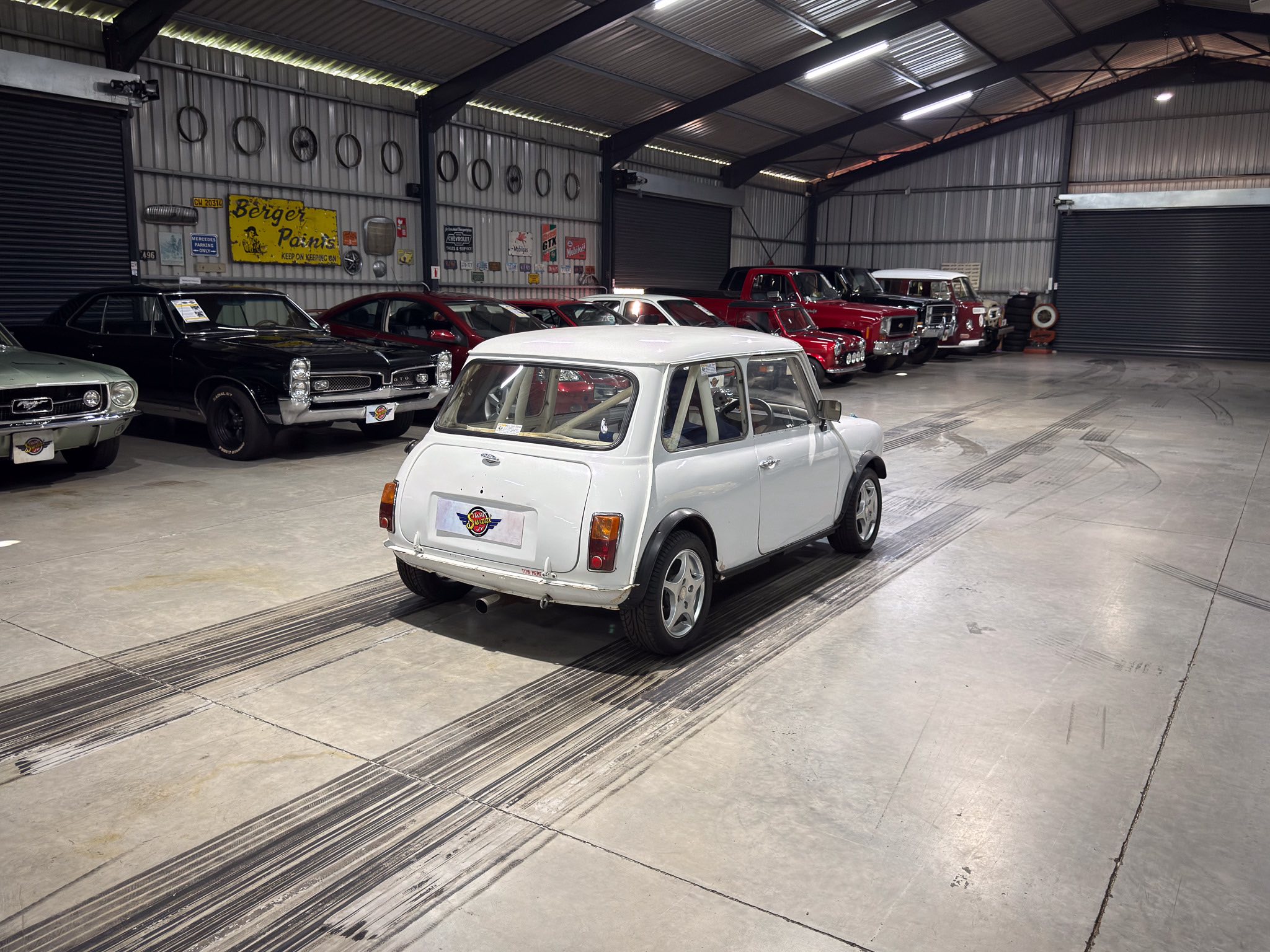 Inside a large metal-walled garage showroom with a row of classic cars on display.
