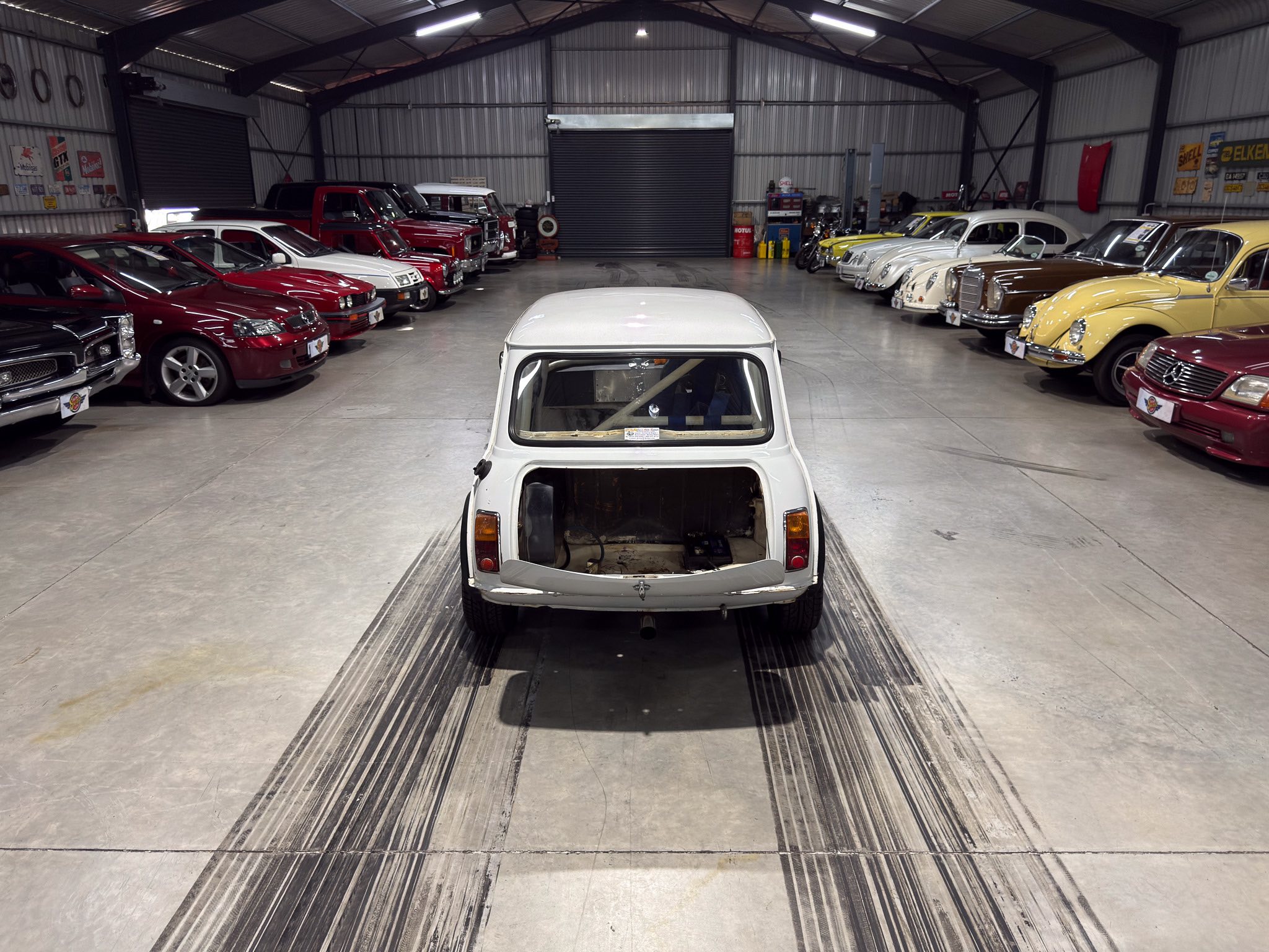 Rear view of a white vintage pickup in a showroom, flanked by rows of classic cars on both sides.