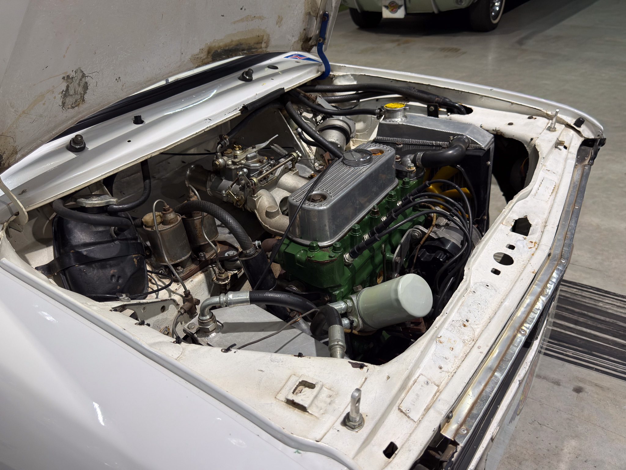 Open car hood revealing the engine bay with hoses, wires, and metallic components in a vintage vehicle