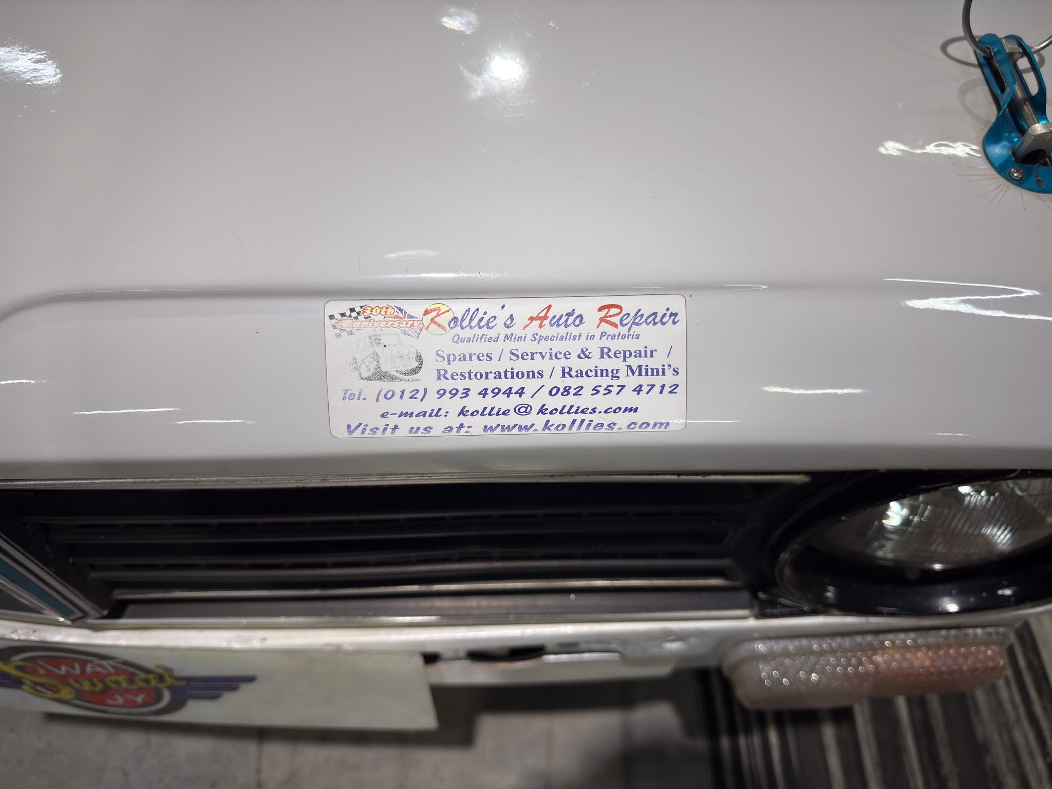 Sticker on a white car bumper advertising Kollie's Auto Repair, with contact info and service notes visible on the plate-style label.