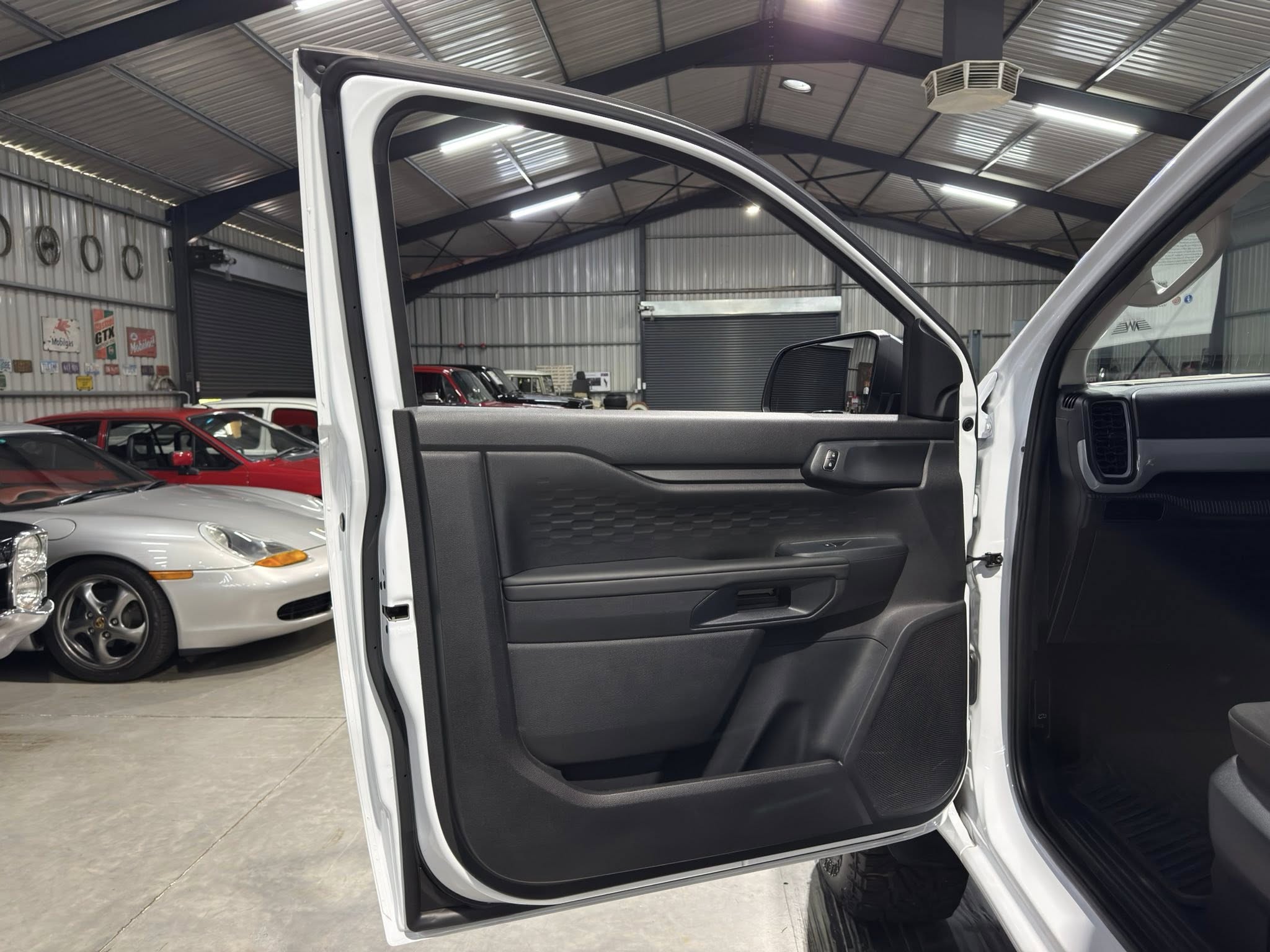 Open car front passenger door inside a busy auto shop with other cars visible in background.