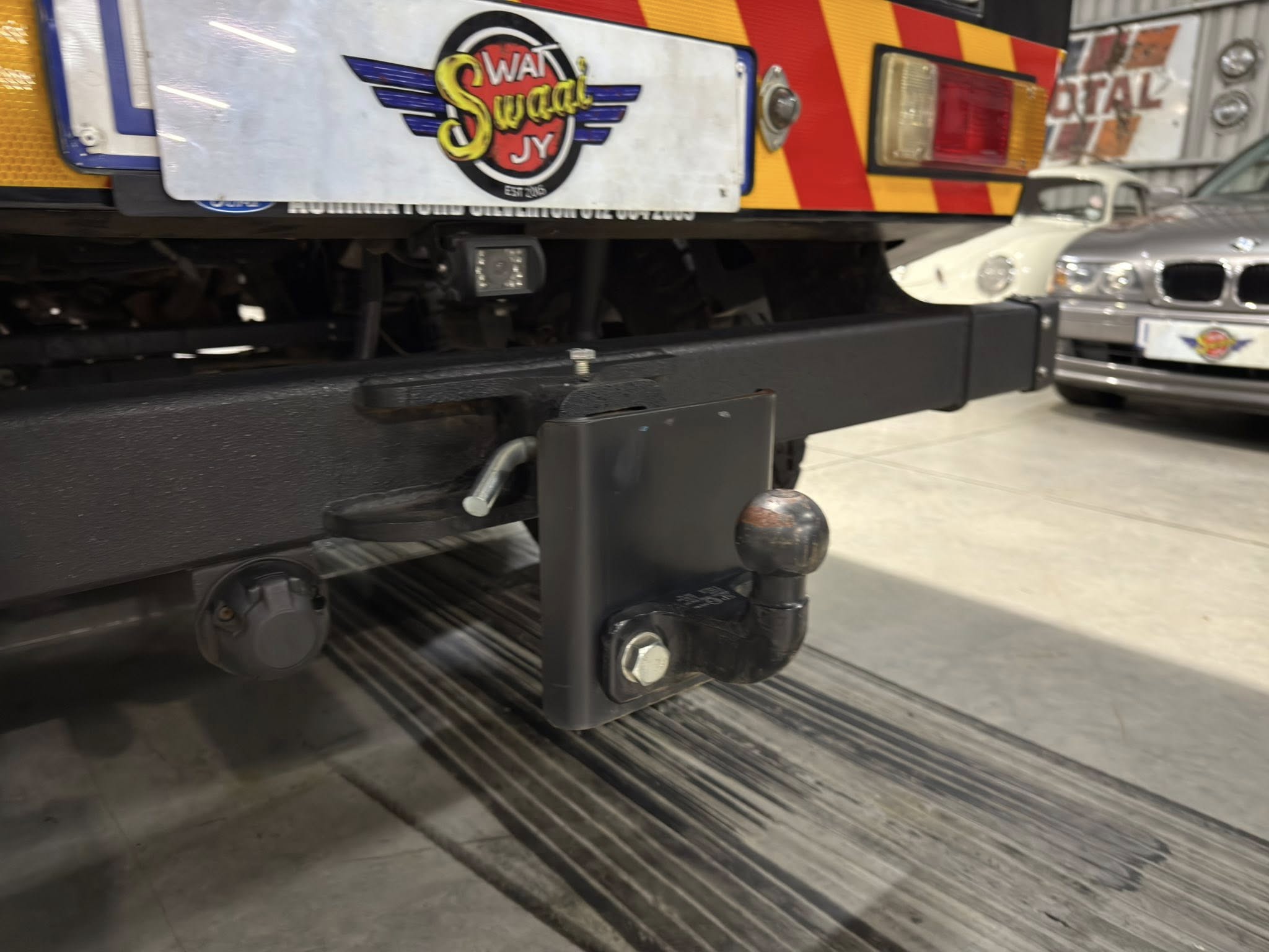 Close-up of a tow truck hitch and undercarriage with a wheel axle visible, showroom floor in background.