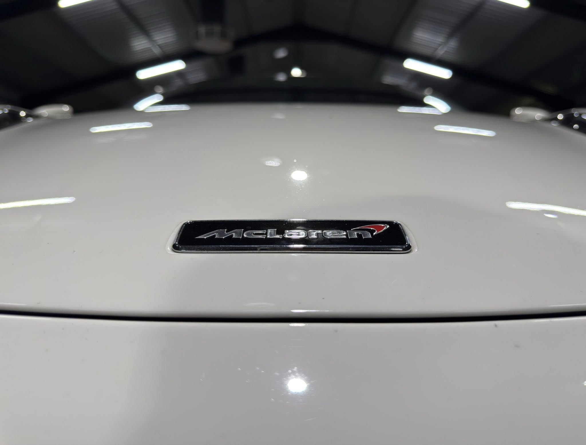 Close-up of a white car hood featuring the black and chrome McLaren emblem in the center of the image.