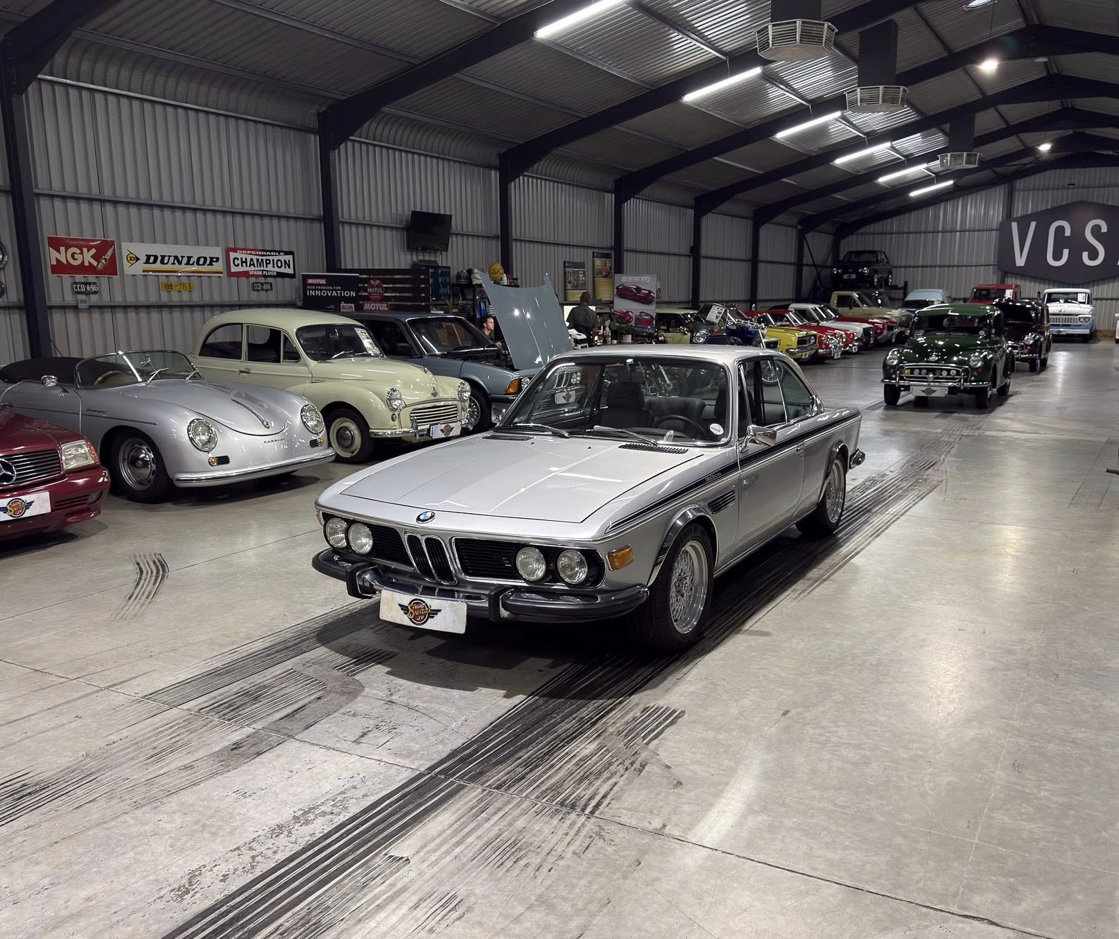 Silver vintage BMW sedan in a showroom surrounded by rows of classic cars.
