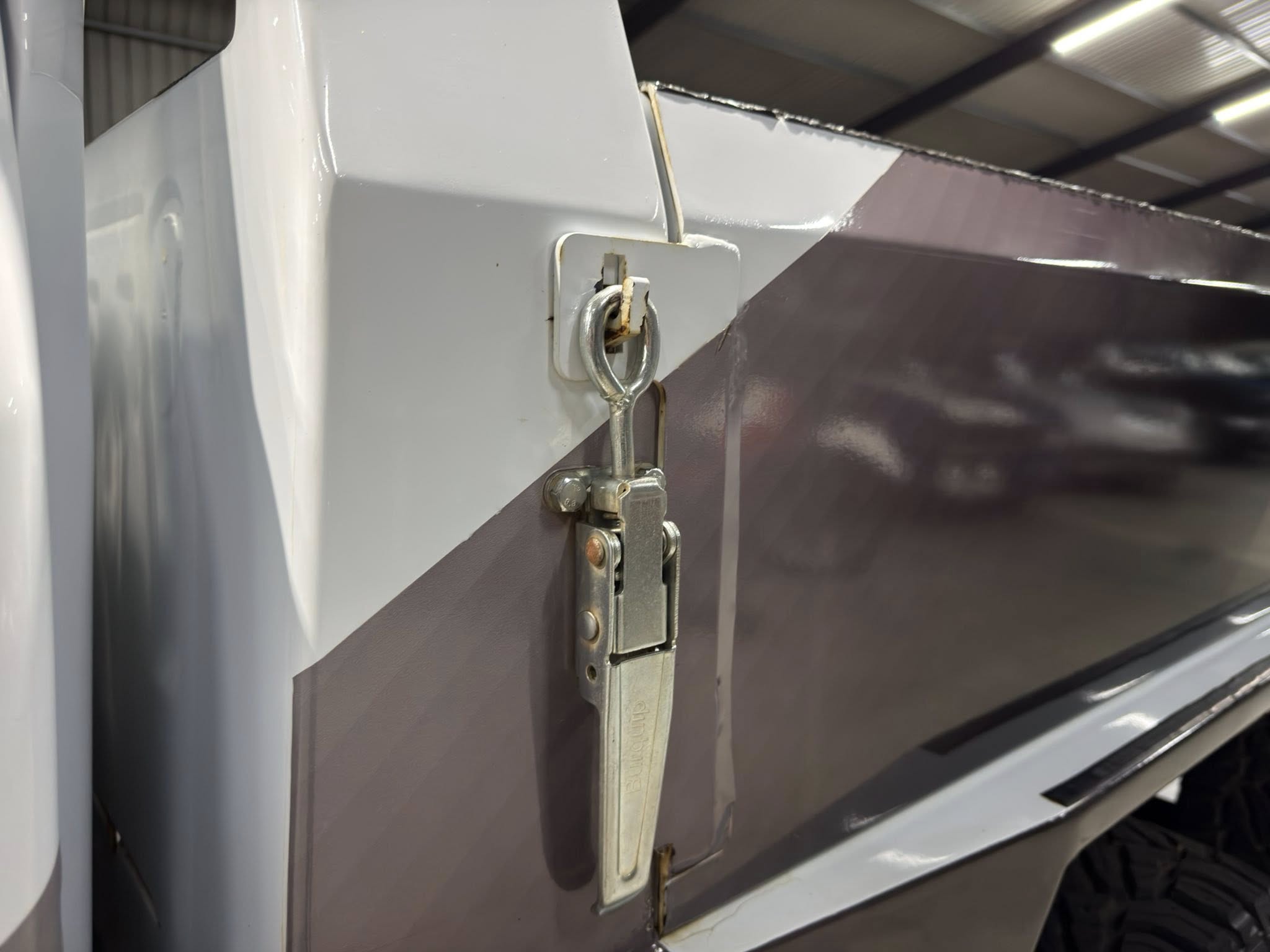 Close-up of a metal hasp and latch securing a gray industrial door panel in a workshop setting.