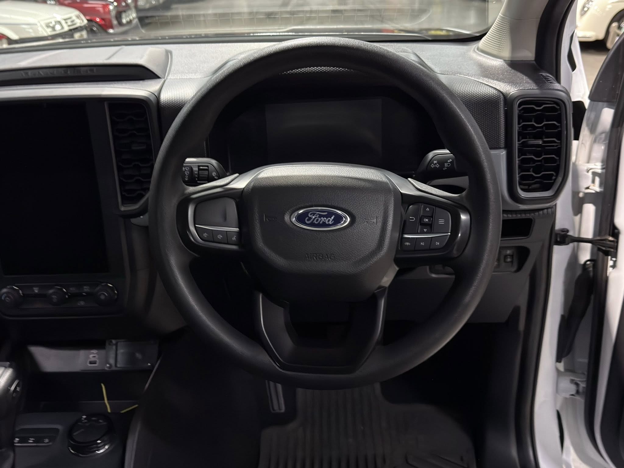 View of a Ford truck dashboard from the driver's seat: steering wheel with controls, large central screen, and vertical air vents on both sides of the dash (left and right).