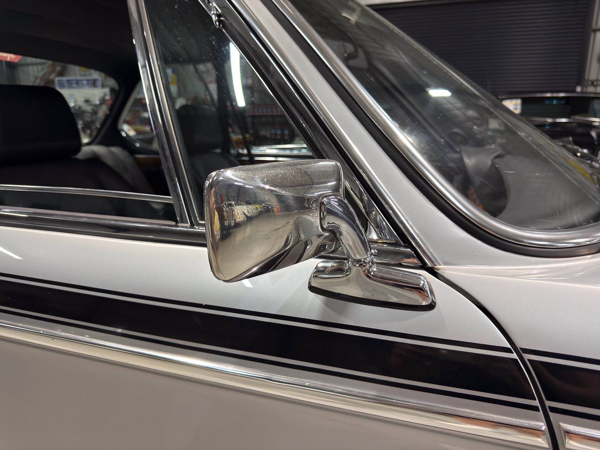 Close-up of a vintage car's chrome side mirror and window trim in a showroom setting.