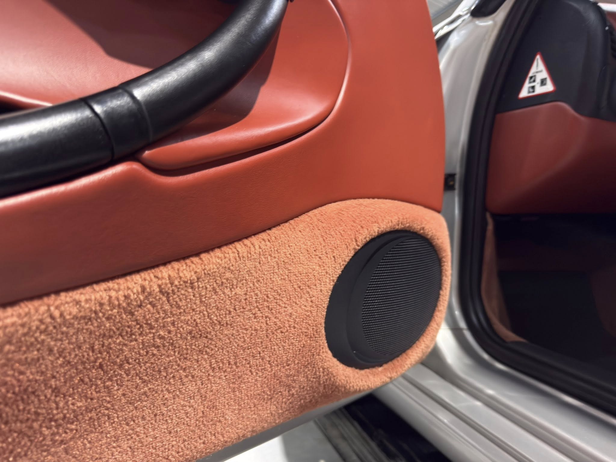 Close-up of orange leather car door panel with a black armrest and round speaker beneath it. (car interior)