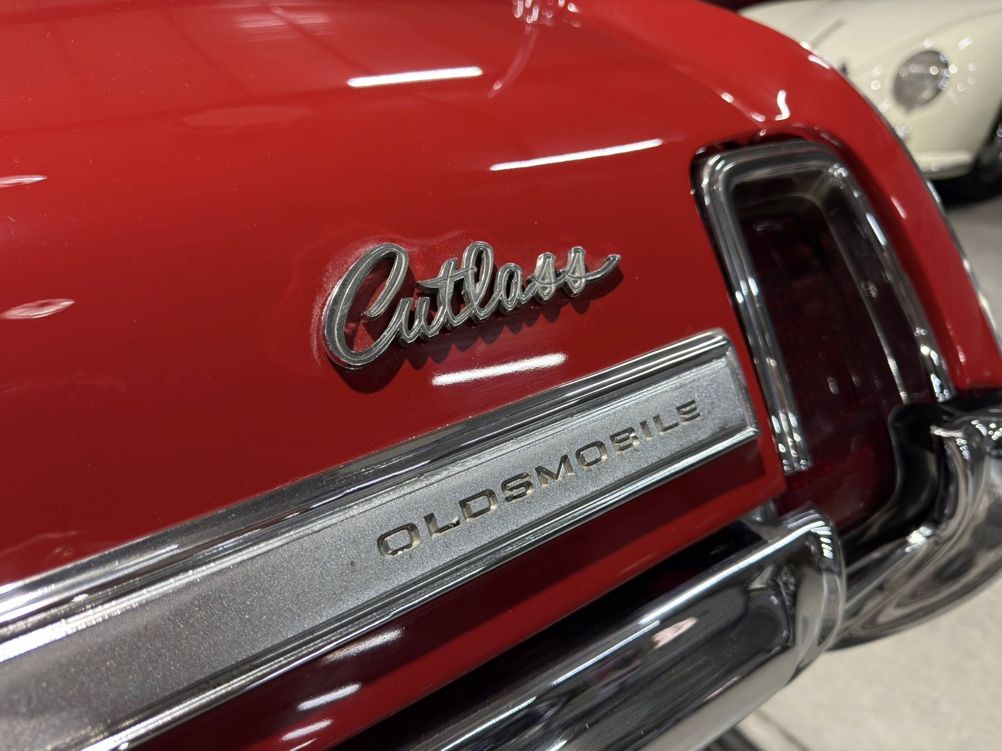Close-up of a red Oldsmobile Cutlass rear badge on the trunk, chrome script reading 'Cutlass' with a chrome bumper below.