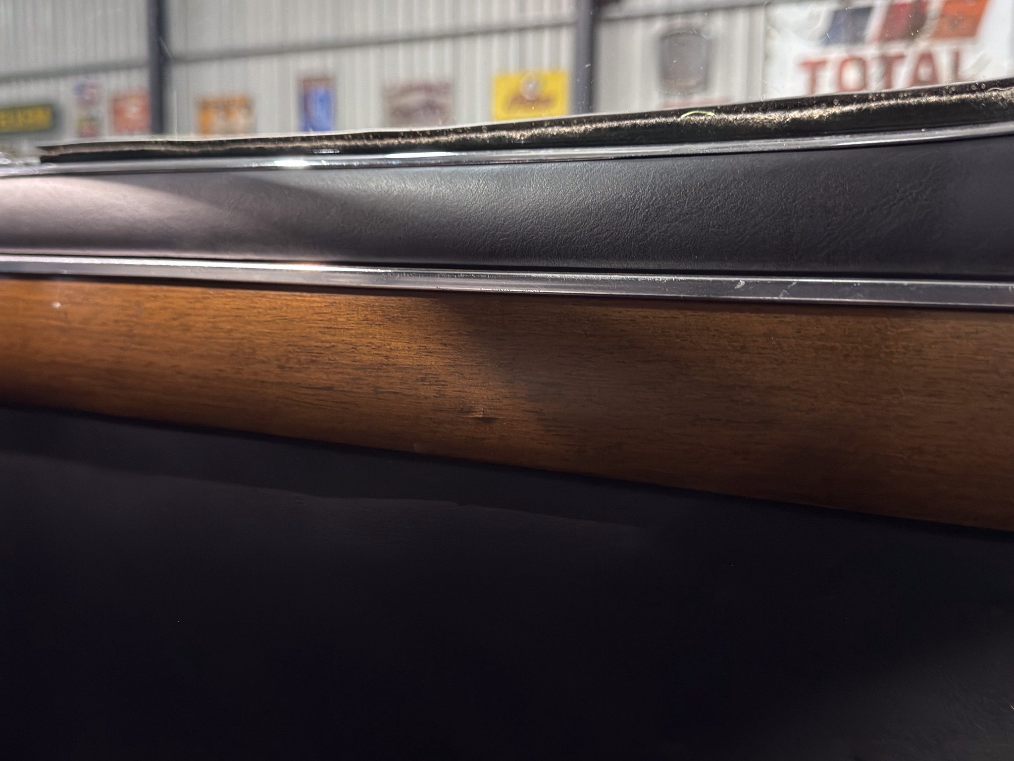 Close-up of a car window frame with black textured dash and wooden trim, a blurred workshop scene in the background