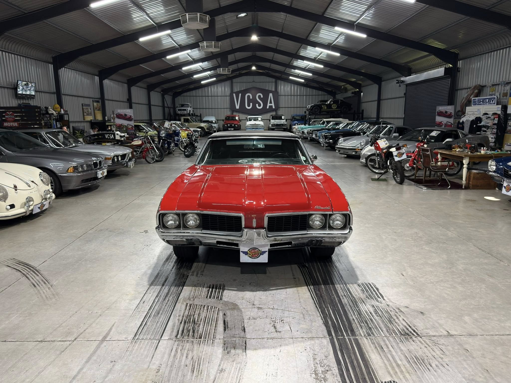 Front view of a red vintage car in a large showroom filled with rows of classic vehicles.