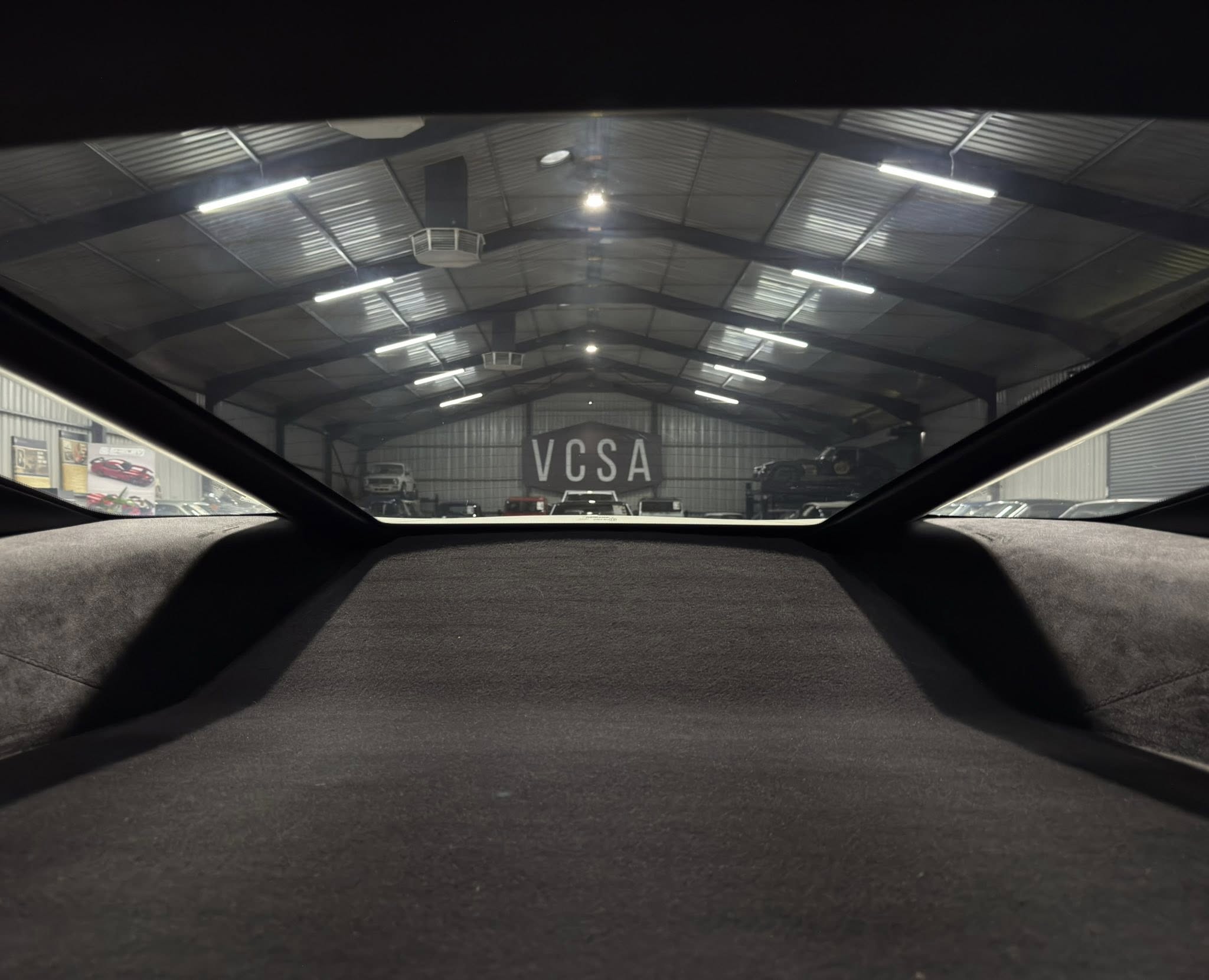 View from inside a car looking into a showroom with a metal roof and a large VCSA sign visible among cars on the floor.