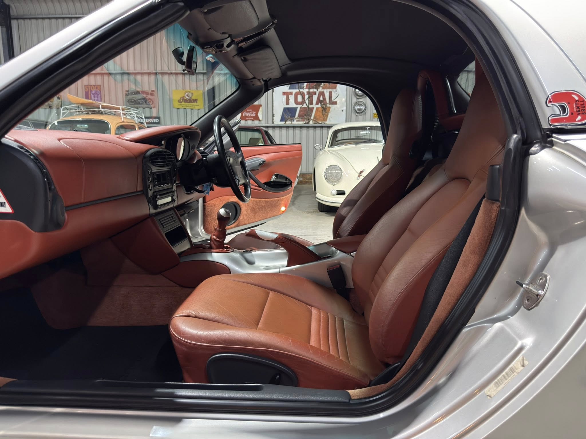 Interior of a silver car with brown leather seats, driver’s door open and dashboard visible.