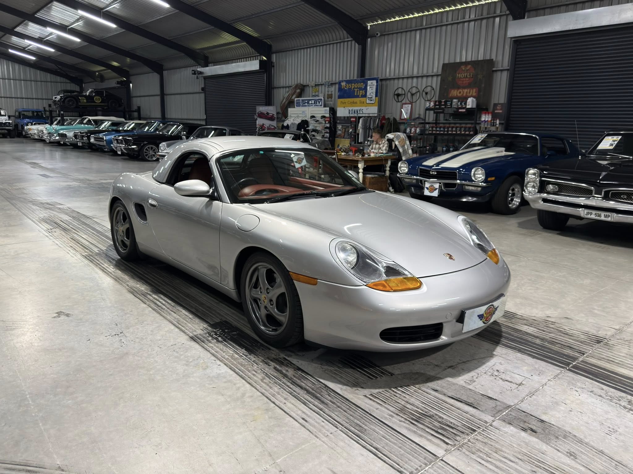 Indoor car showroom with a row of vintage and modern cars, the silver Porsche in the foreground stands out.