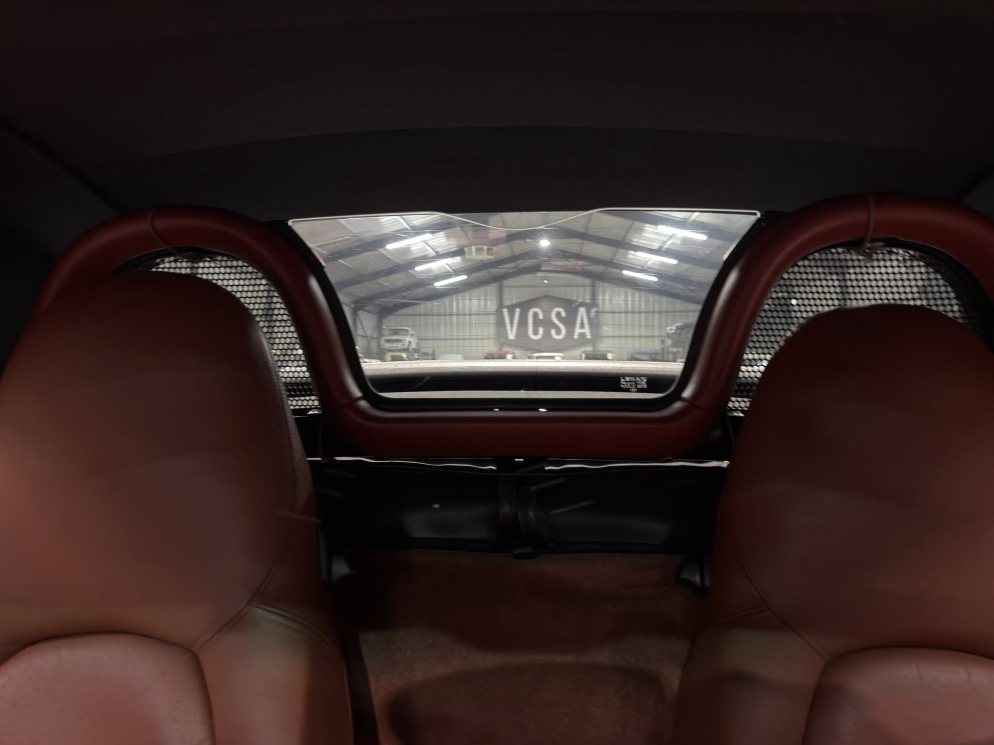 Back view from inside a car with red leather seats, open hatch reveals a garage with 'VCSA' on the wall.