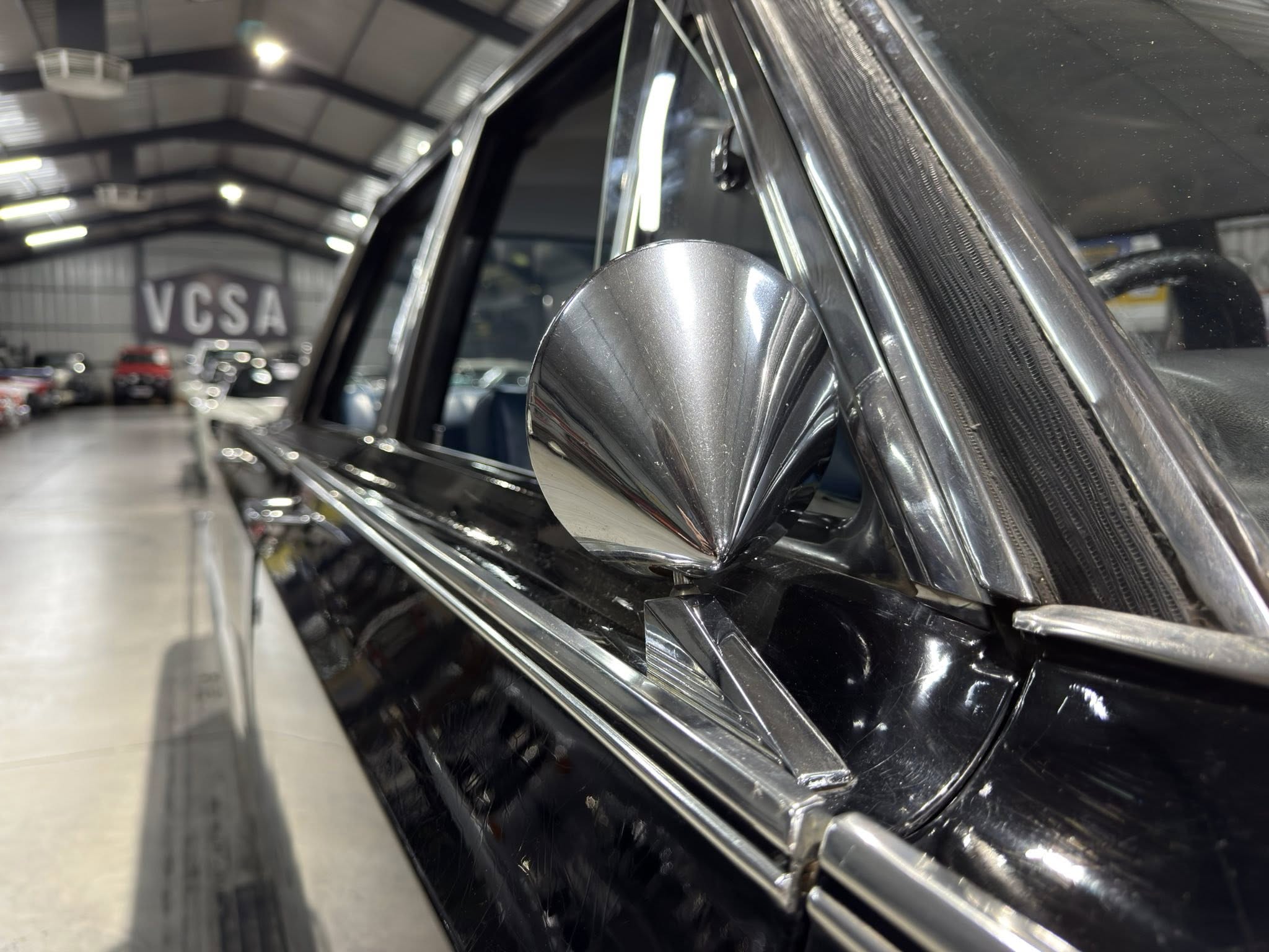 Close-up of chrome trim and side mirror on a black car, with a showroom interior blurred in the background.