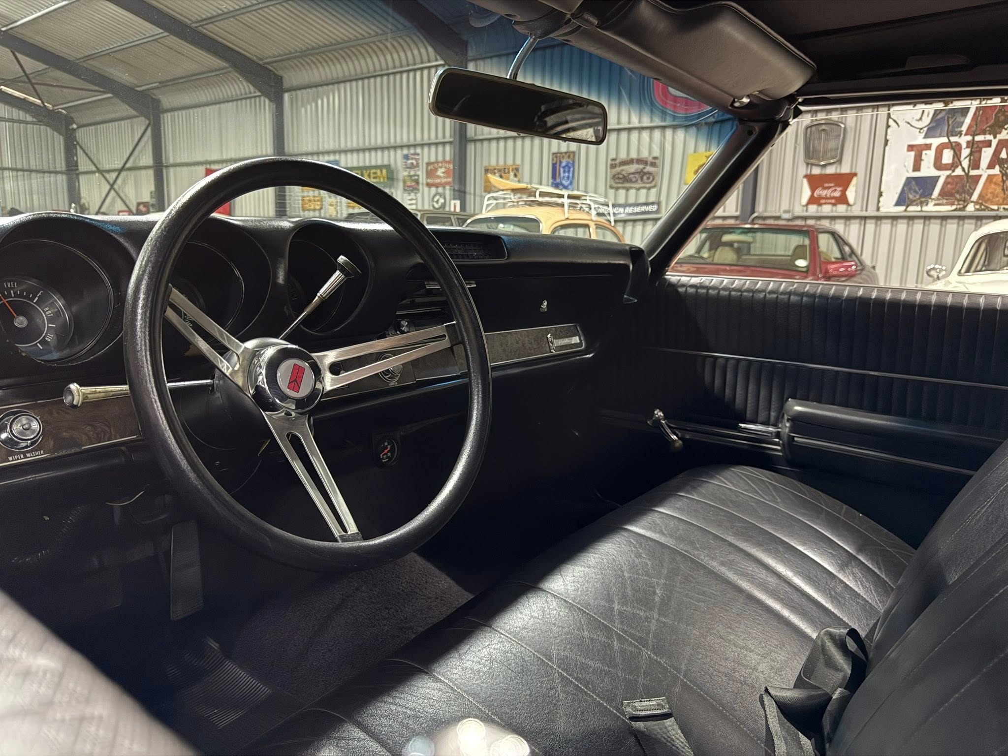 Interior of a classic car: black leather seats, large circular steering wheel, and vintage dashboard.