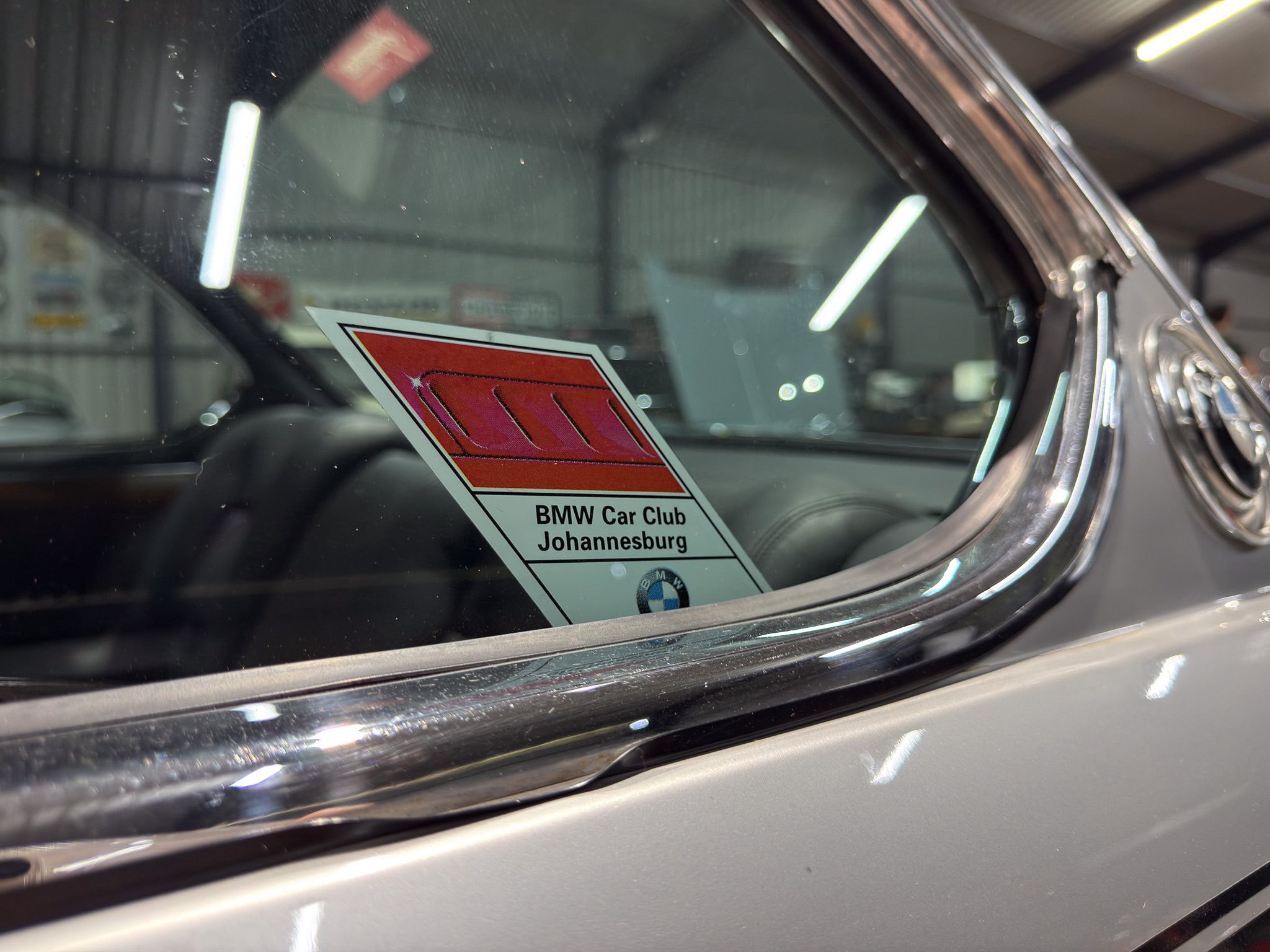 Close-up of a car windshield with a BMW Car Club Johannesburg sticker attached to the glass.