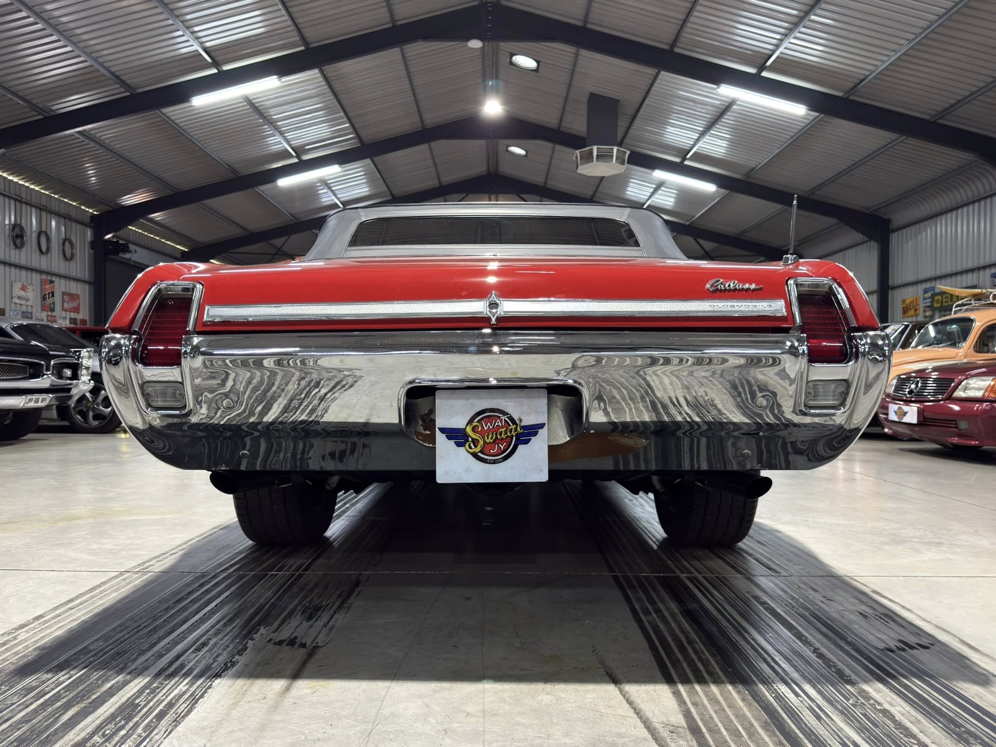 Rear view of a red vintage Cadillac convertible with chrome bumper and gray soft top inside a car showroom. Other classic cars line the sides.