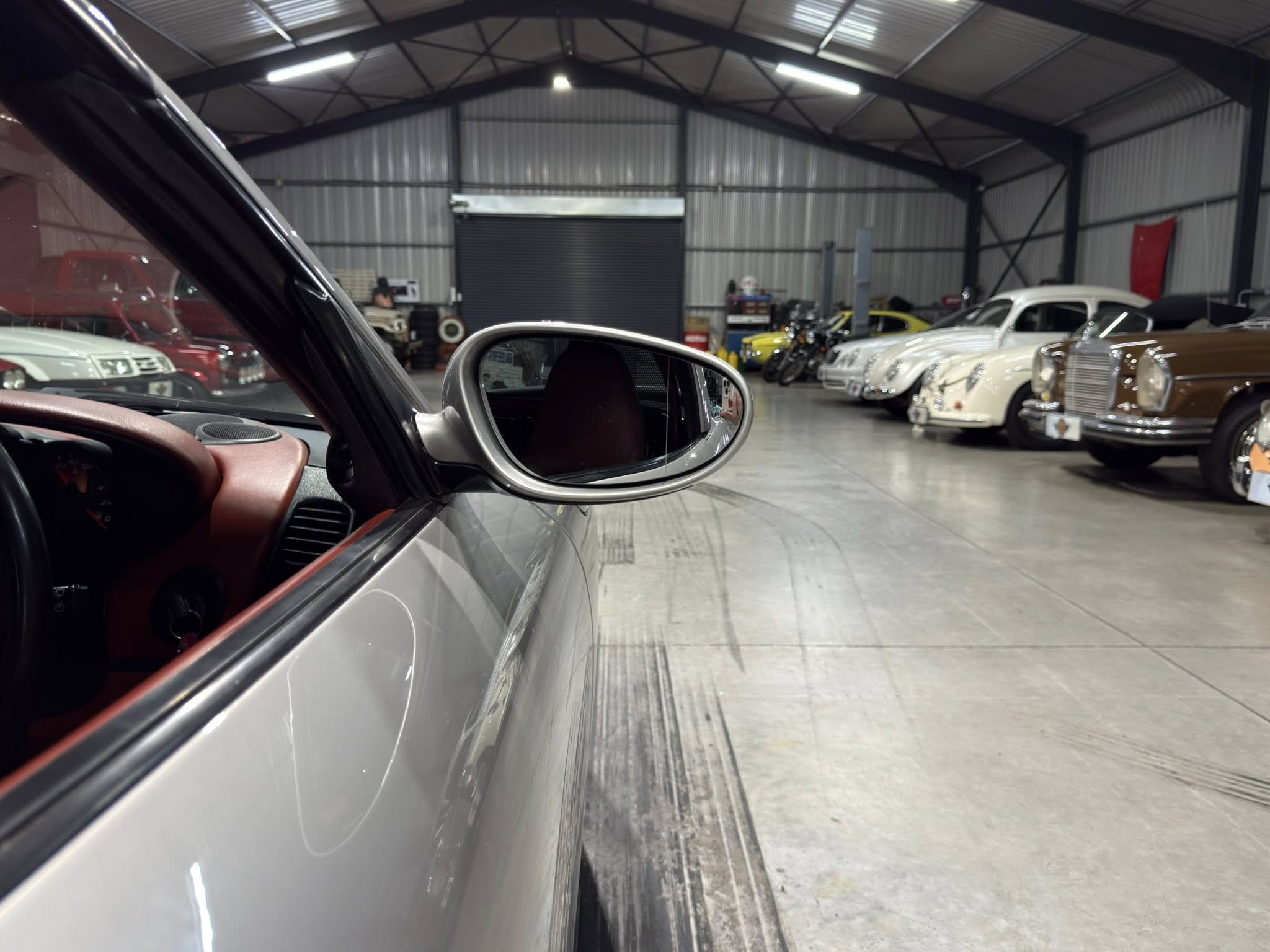 Perspective from inside a car looking at a row of vintage cars in a showroom.
