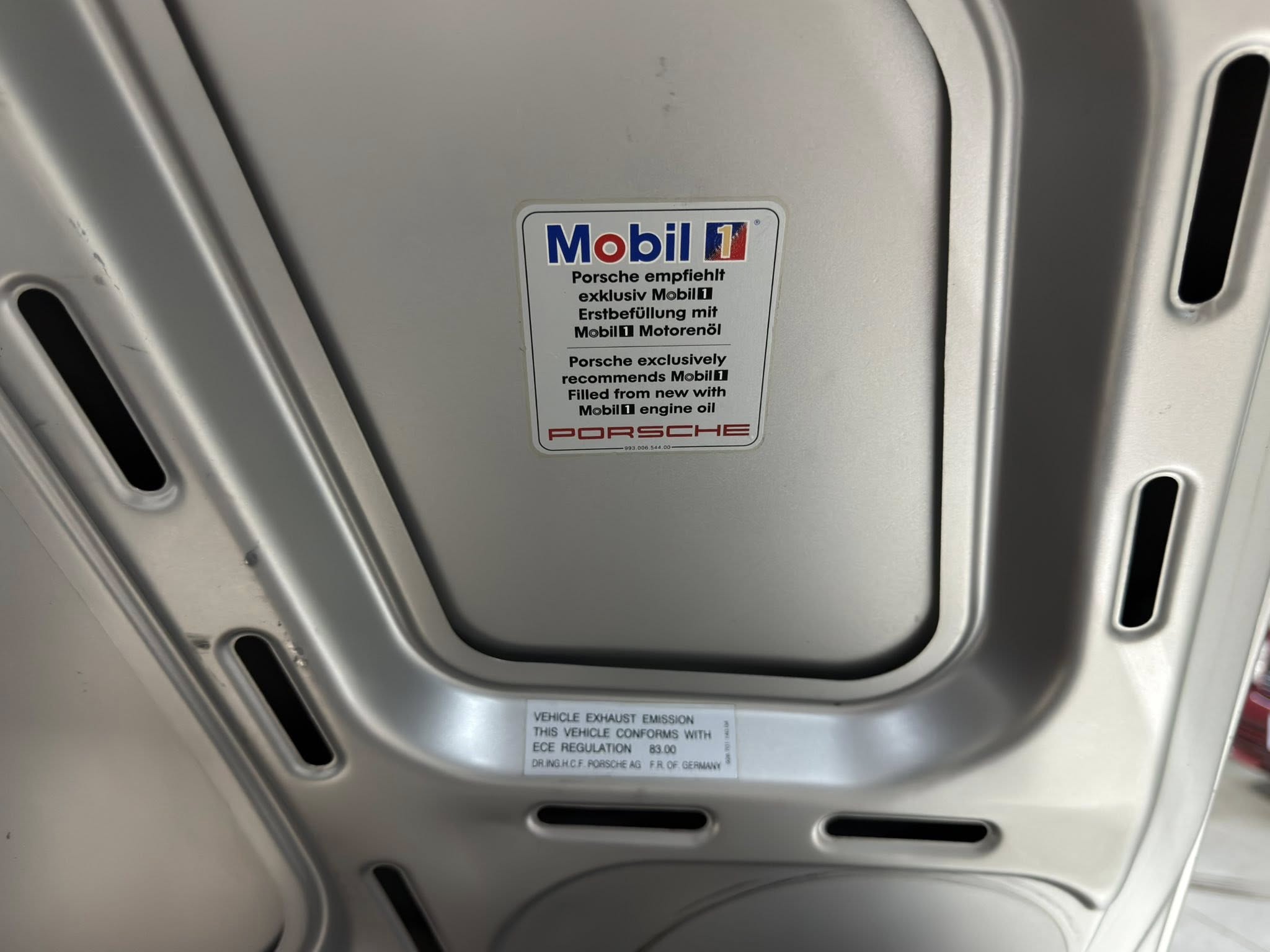 Close-up of a Porsche hood area with a Mobil 1 sticker and oil recommendation label on the underside of the hood.