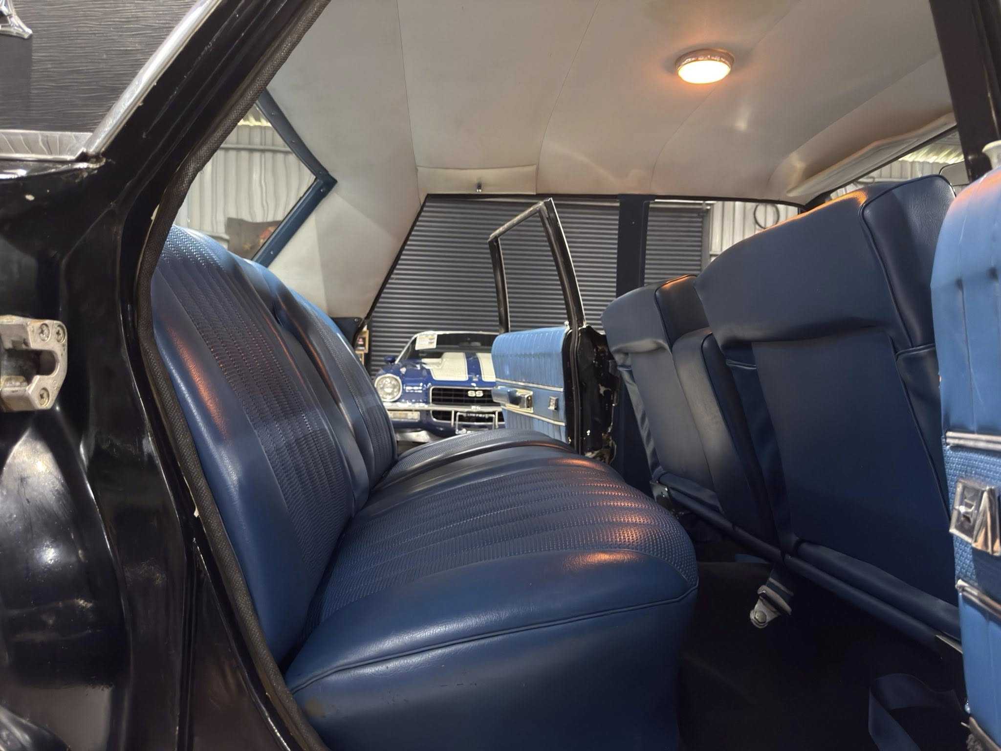 Interior of a blue vintage car with two rows of blue upholstered seats and a central aisle, in a garage setting.