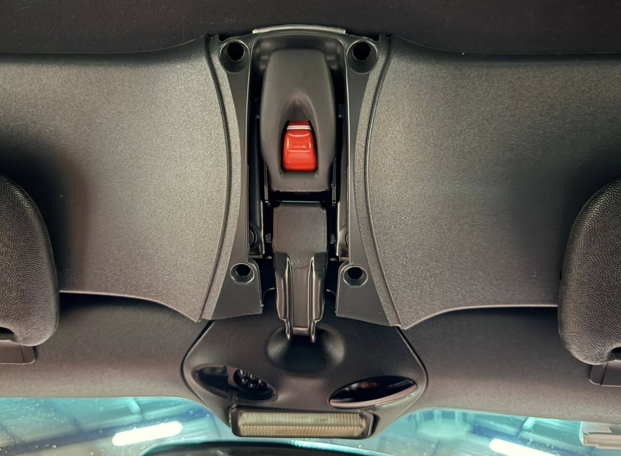 Close-up of a car's overhead console with a red release lever in the center between dark plastic housings