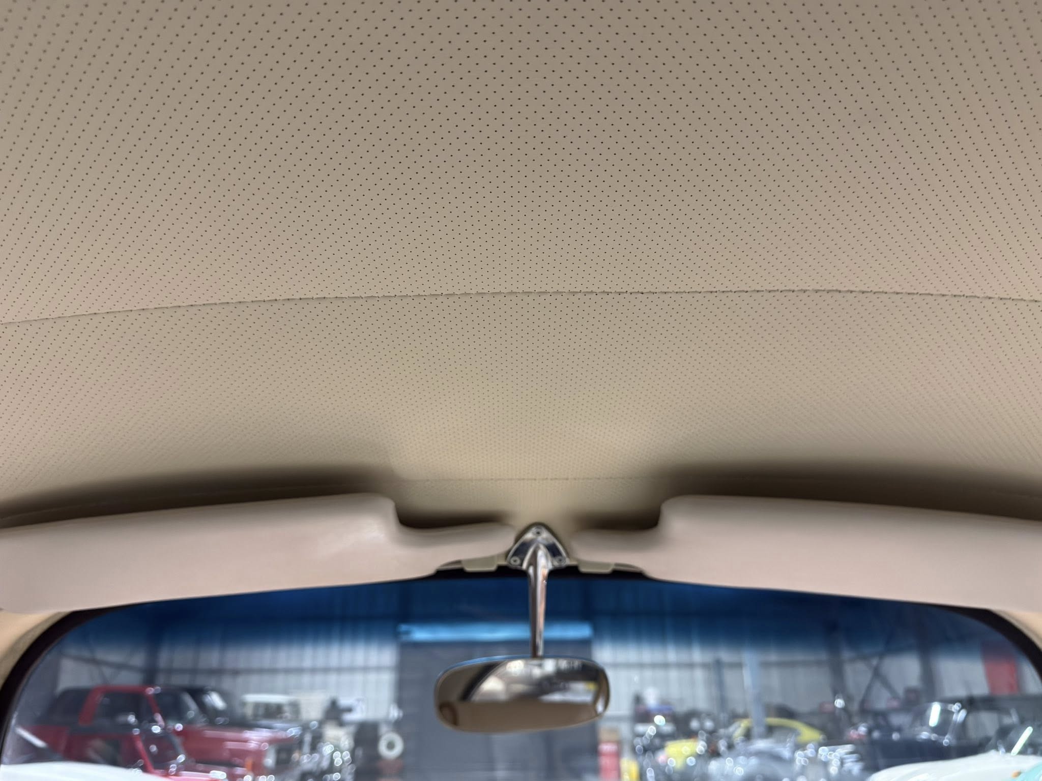 Interior of a car viewed from the back seat, showing the dotted headliner and a central rearview mirror with a blurred parking lot outside the windshield.