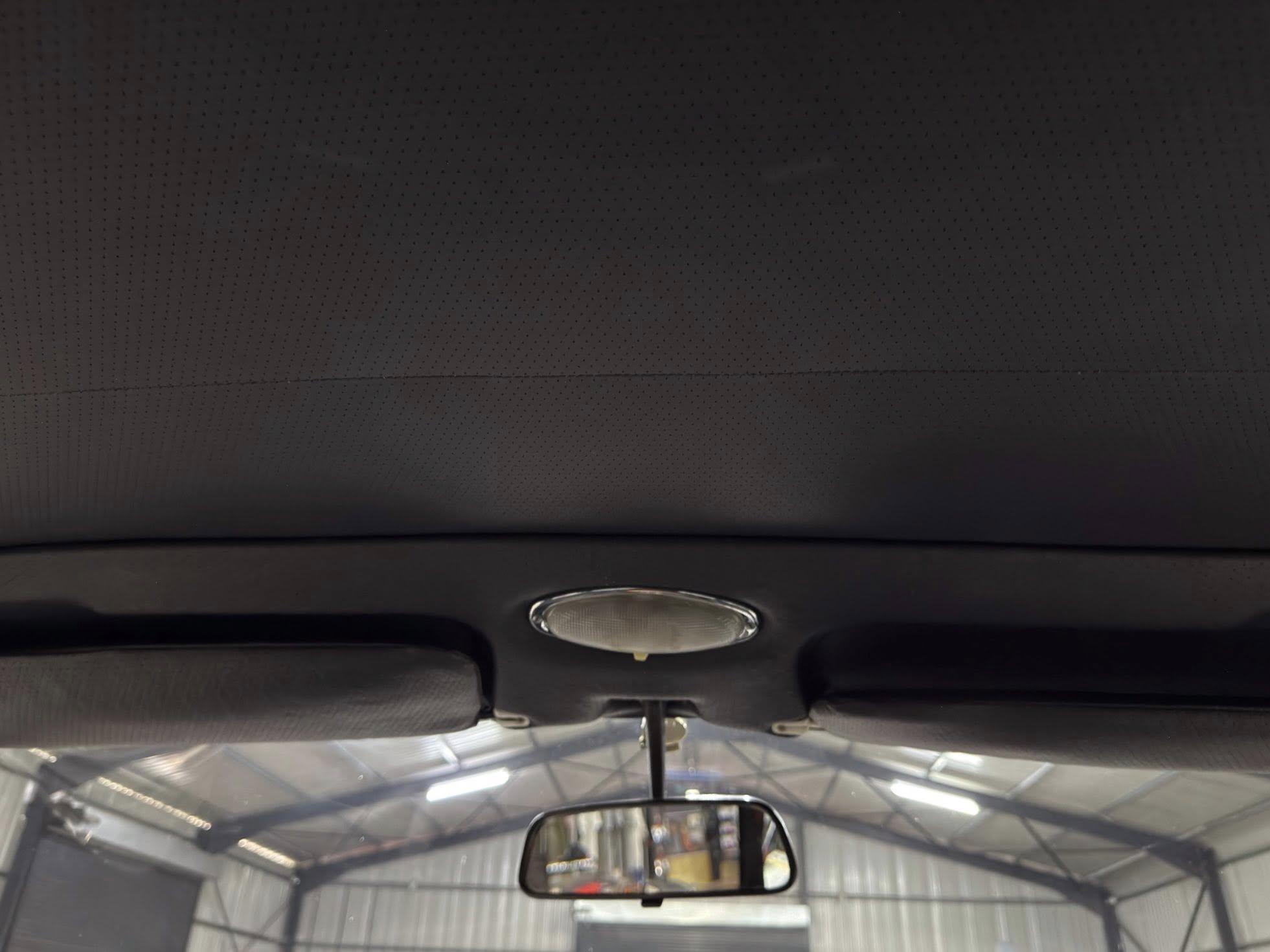 Interior of a car viewed from the back seat, showing the dotted headliner, overhead dome light, and rearview mirror reflecting the showroom outside.