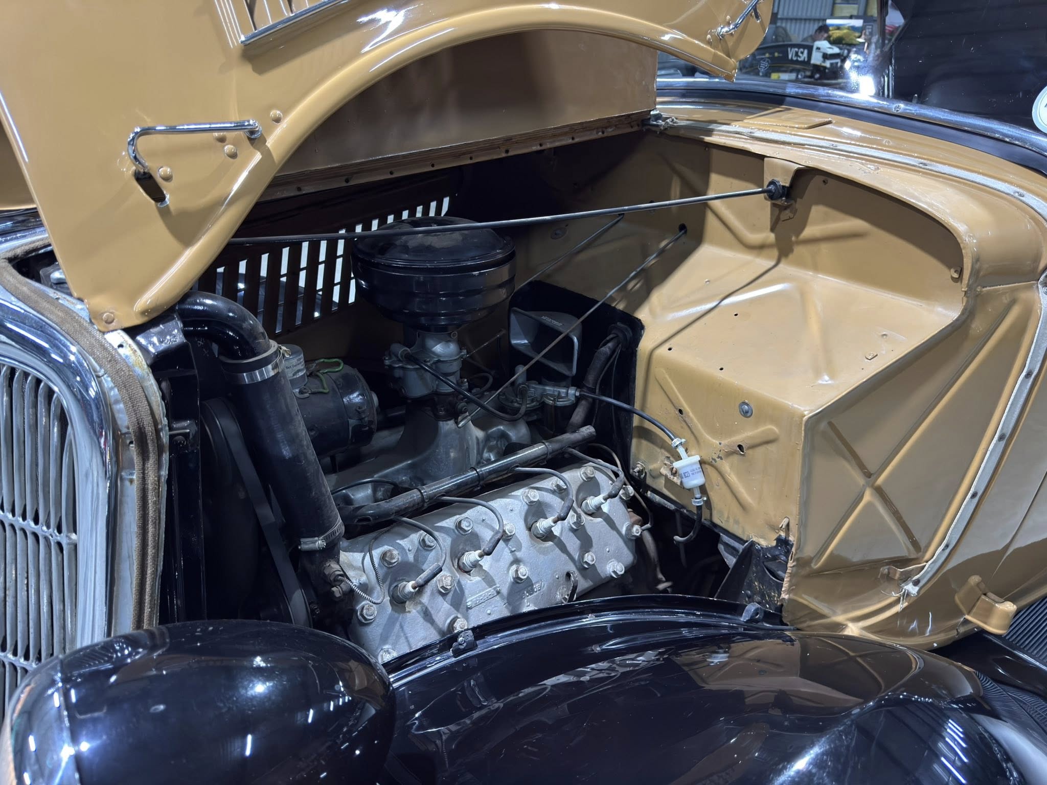 Open car hood reveals a classic V8 engine with gold-painted body and vintage components.