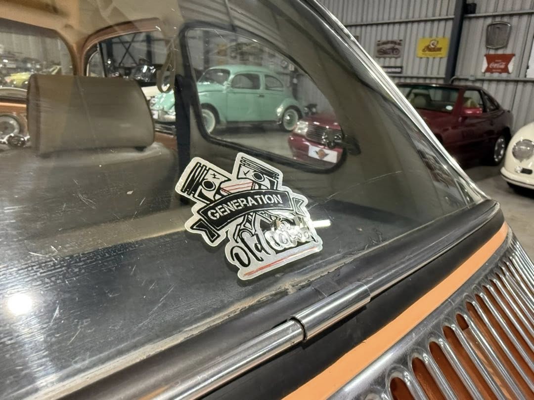 Sticker on the windshield reading 'Generation Old School' with a piston graphic, in a garage full of vintage cars in the background.