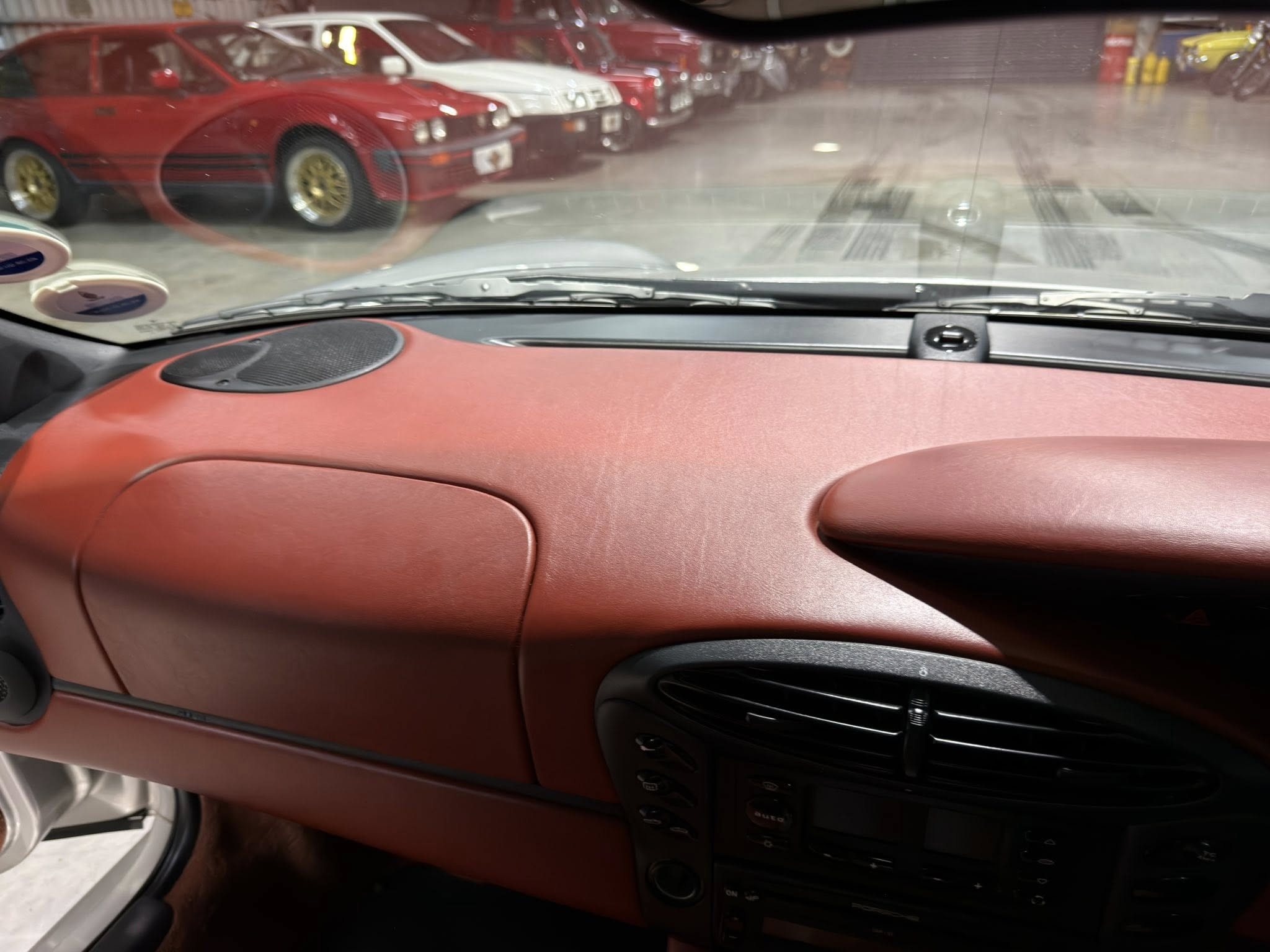 Red leather car dashboard and center console with windshield showing a row of red cars in a showroom outside.