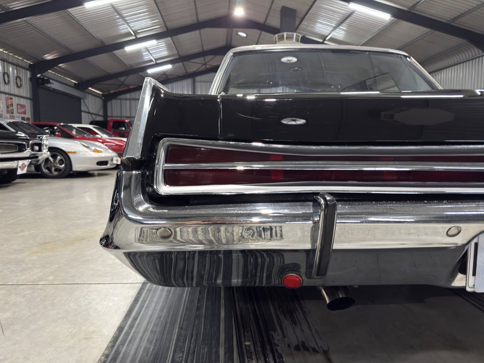 Close-up of the rear end of a black vintage car in a showroom with other colorful cars in the background.