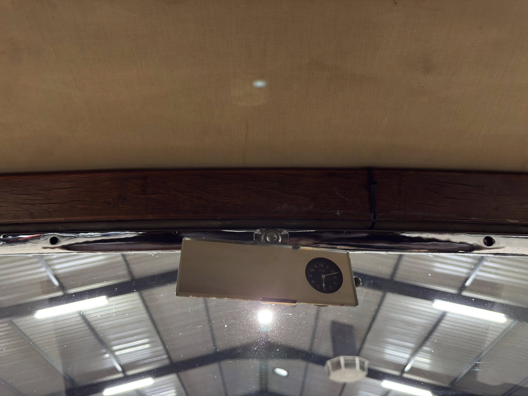 Upside-down interior view showing a brown wall panel above a dark wooden beam, with a small metal panel featuring a round gauge in the foreground and a glass ceiling with metal framing.