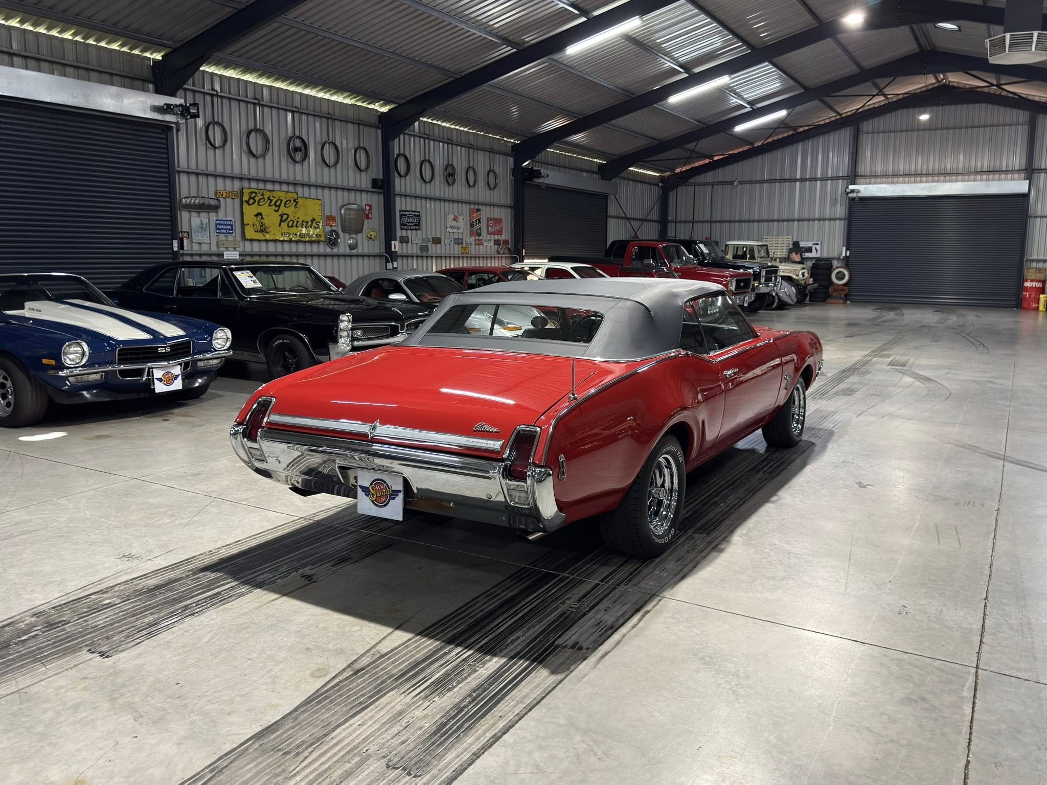 Indoor showroom with several classic vintage cars parked side by side in a large metal warehouse.