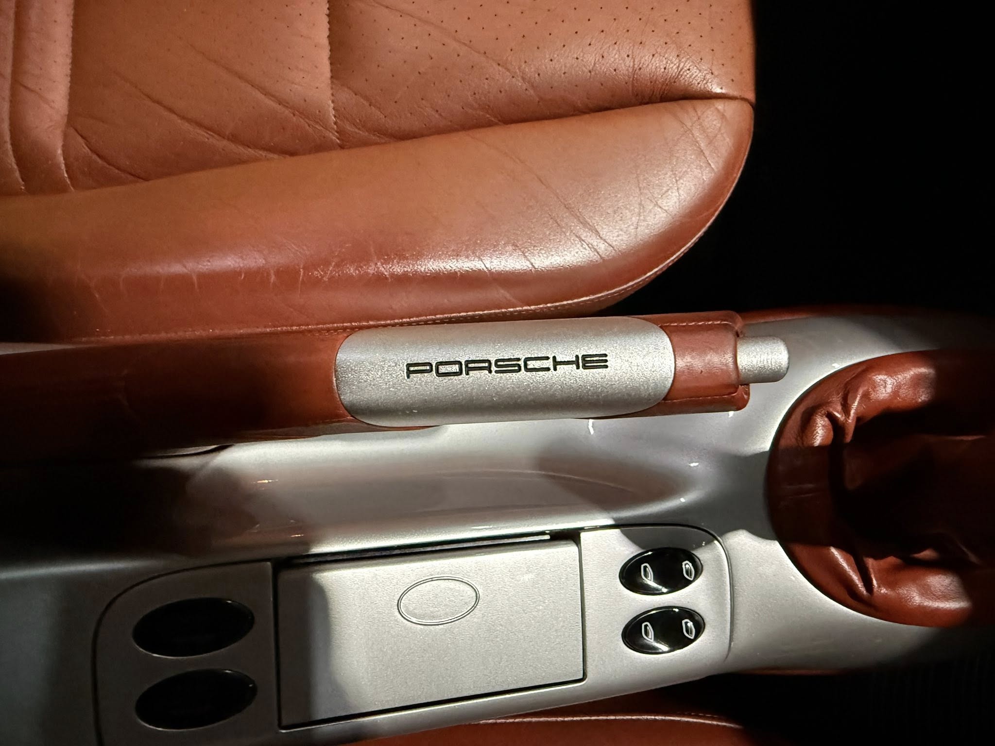 Close-up of red leather car interior showing a silver armrest with the word PORSCHE embossed/printed on it.
