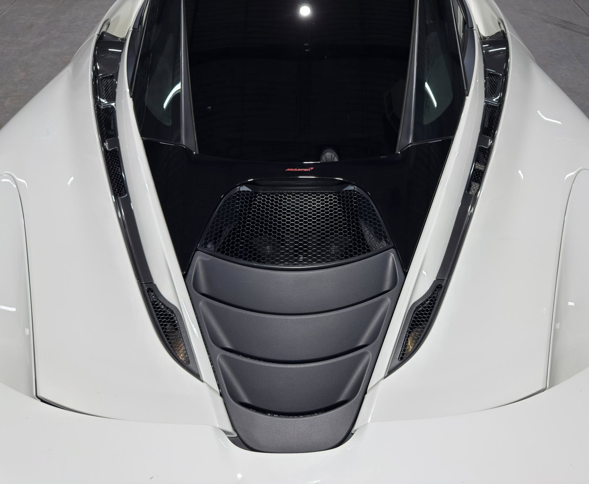 Top-down view of a white McLaren sports car, focusing on the cockpit opening and front intake with mesh grille on each side.