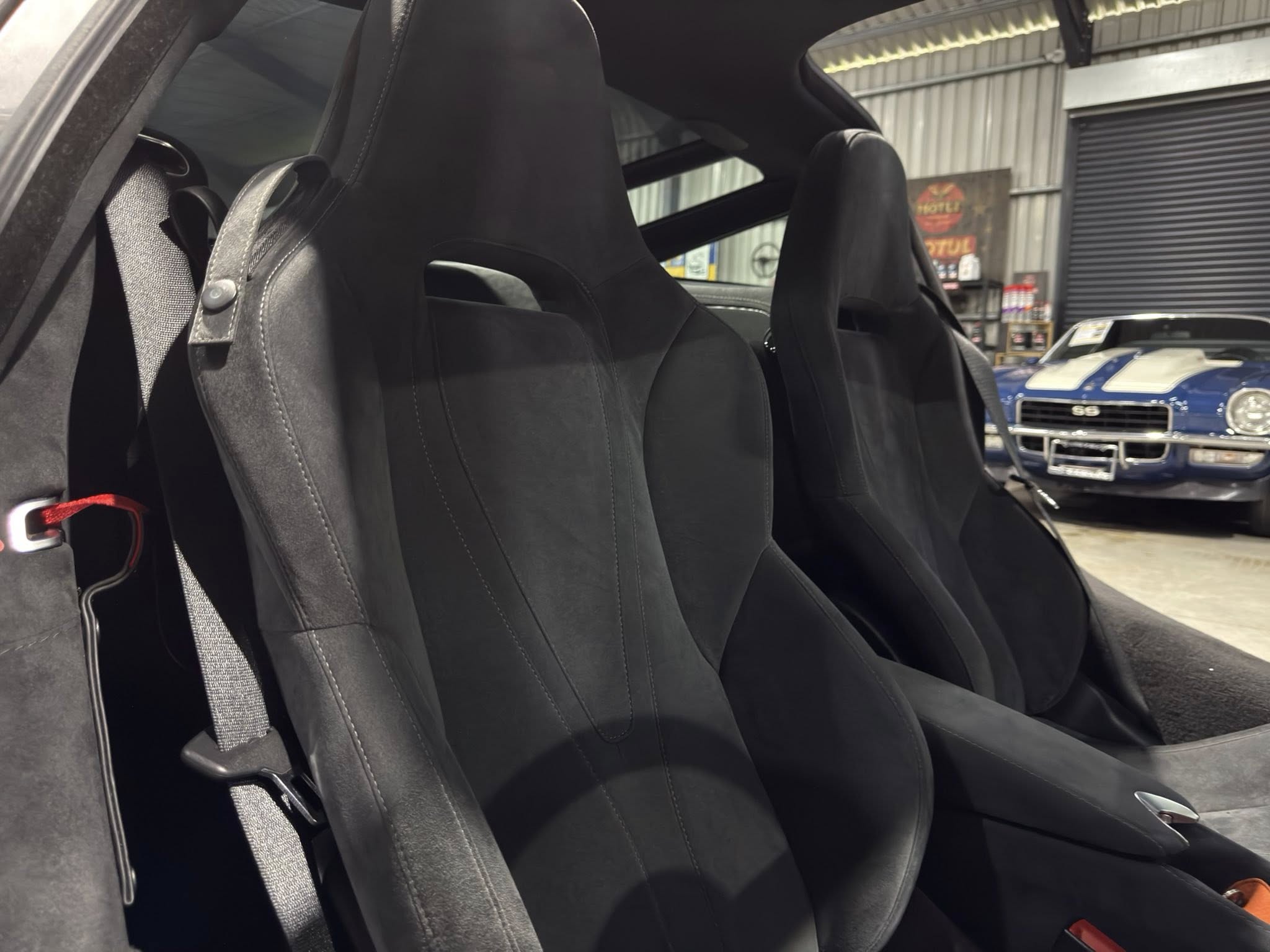 Close-up of black leather sport seats and a gray seat belt in a car with its top down, parked in a garage.
