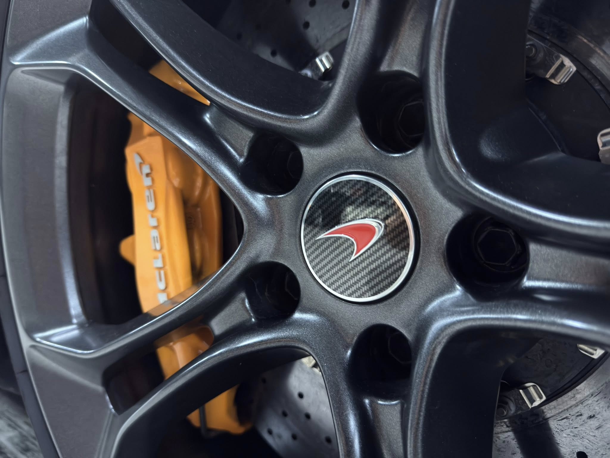 Close-up of a car interior showing a carbon-fiber center panel and a bright orange component with white lettering partially visible behind the panel.