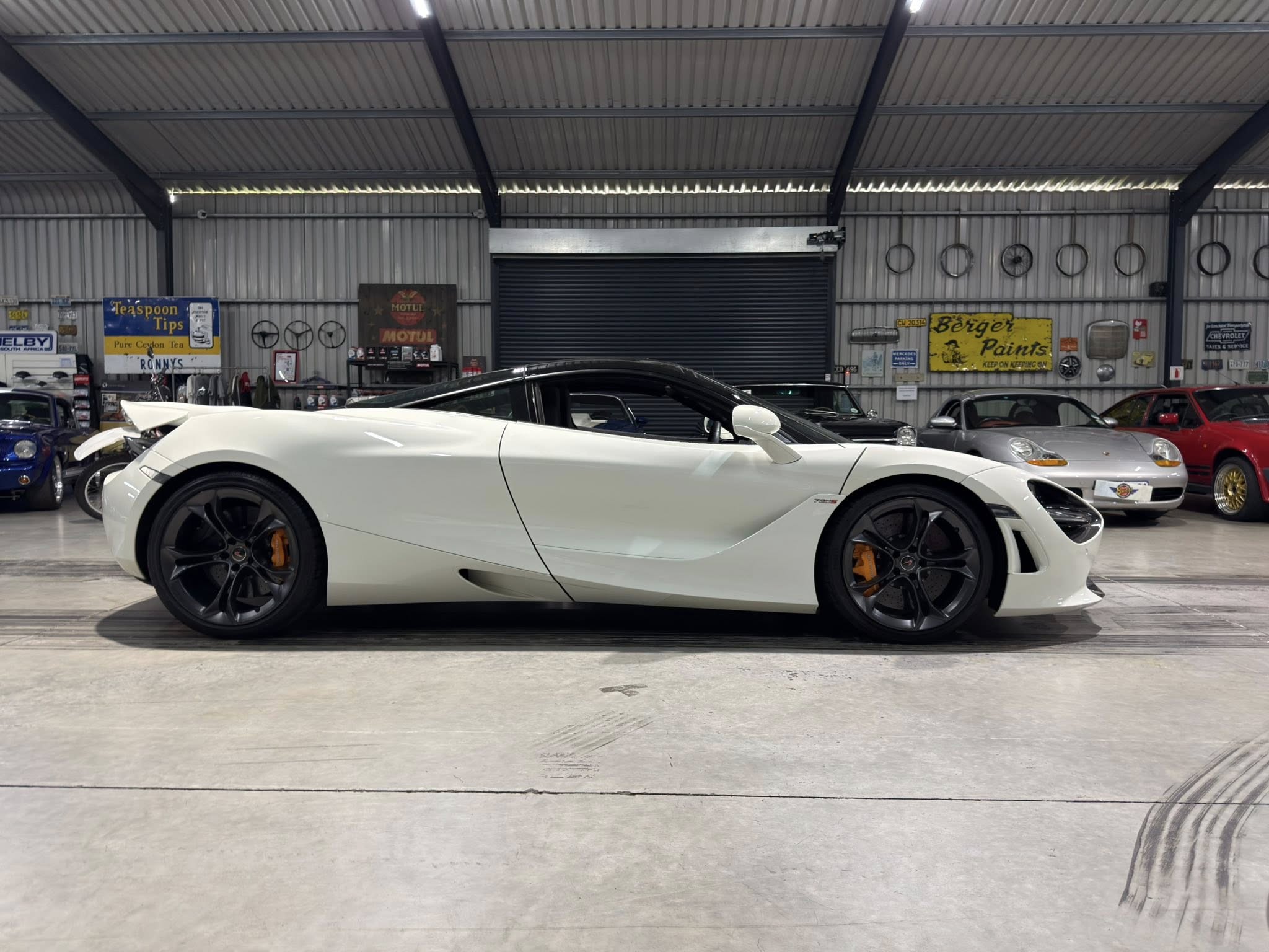 White luxury sports car parked indoors in a garage with metal walls and vintage signs on display in the background