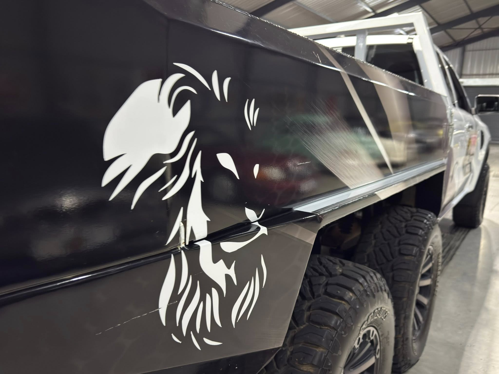 Close-up of a black truck side with a white decorative graphic, with rugged tires visible in a workshop.