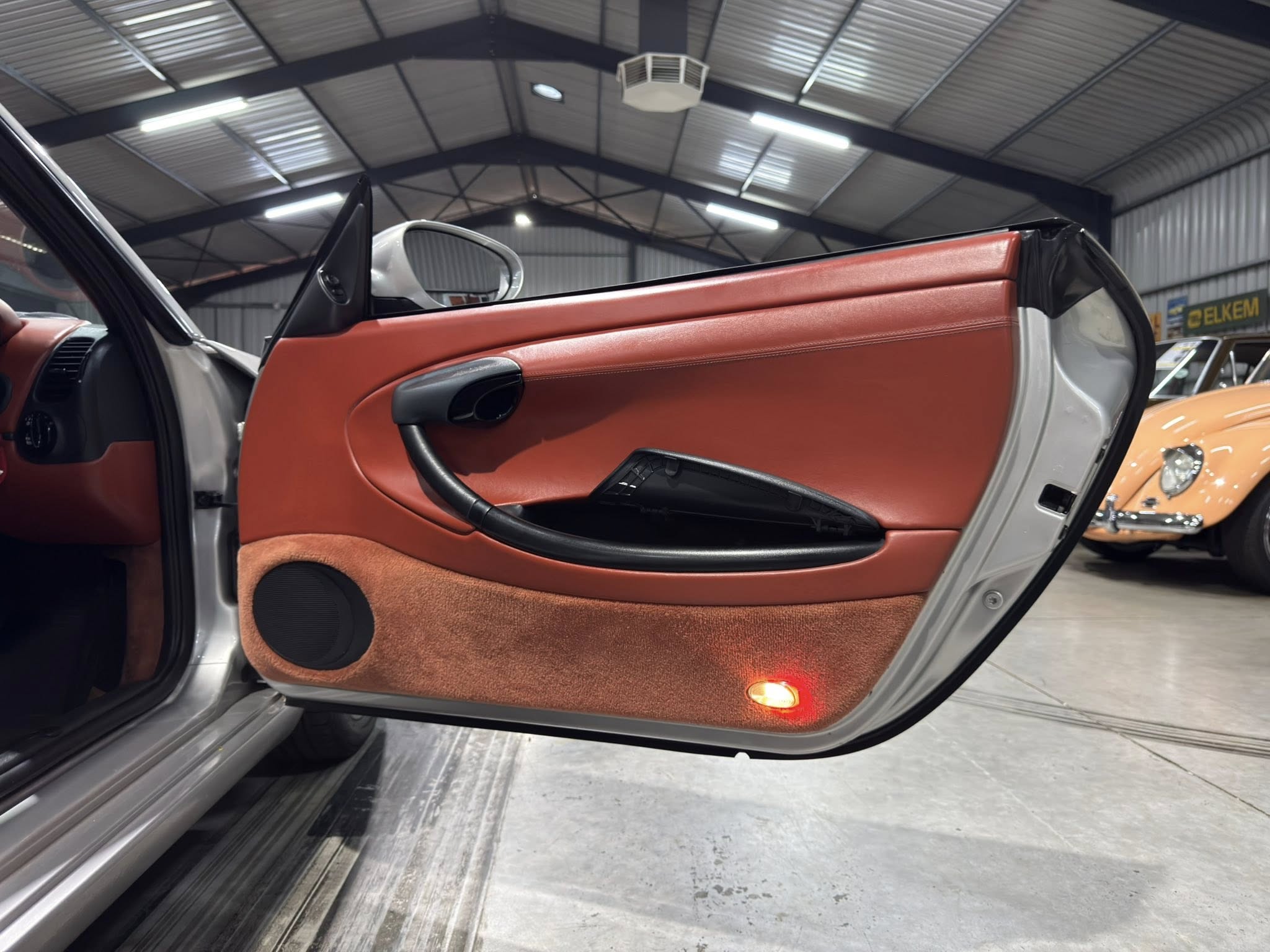 Open red-orange car door in a showroom, showing the interior door panel and orange carpeting.