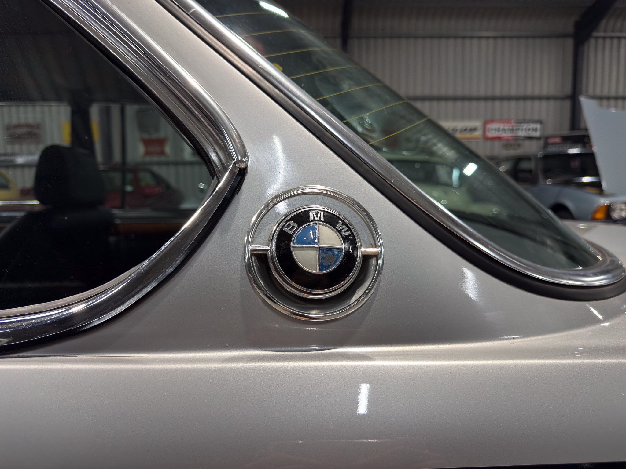 Close-up of a vintage BMW badge on a silver car with chrome trim, inside a garage.