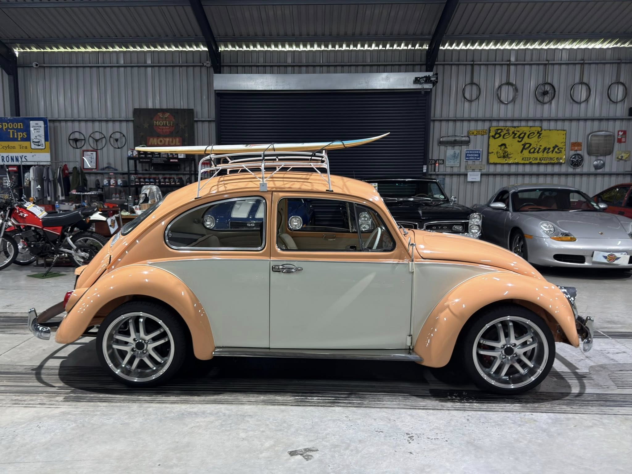 Two-tone vintage car with a wooden boat secured on its roof rack inside a garage filled with auto memorabilia and tools