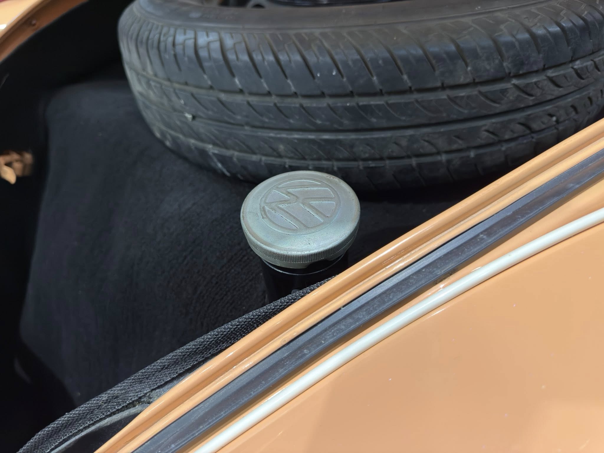 Spare tire secured in the trunk with a Volkswagen wheel center cap resting nearby on the trunk floor.