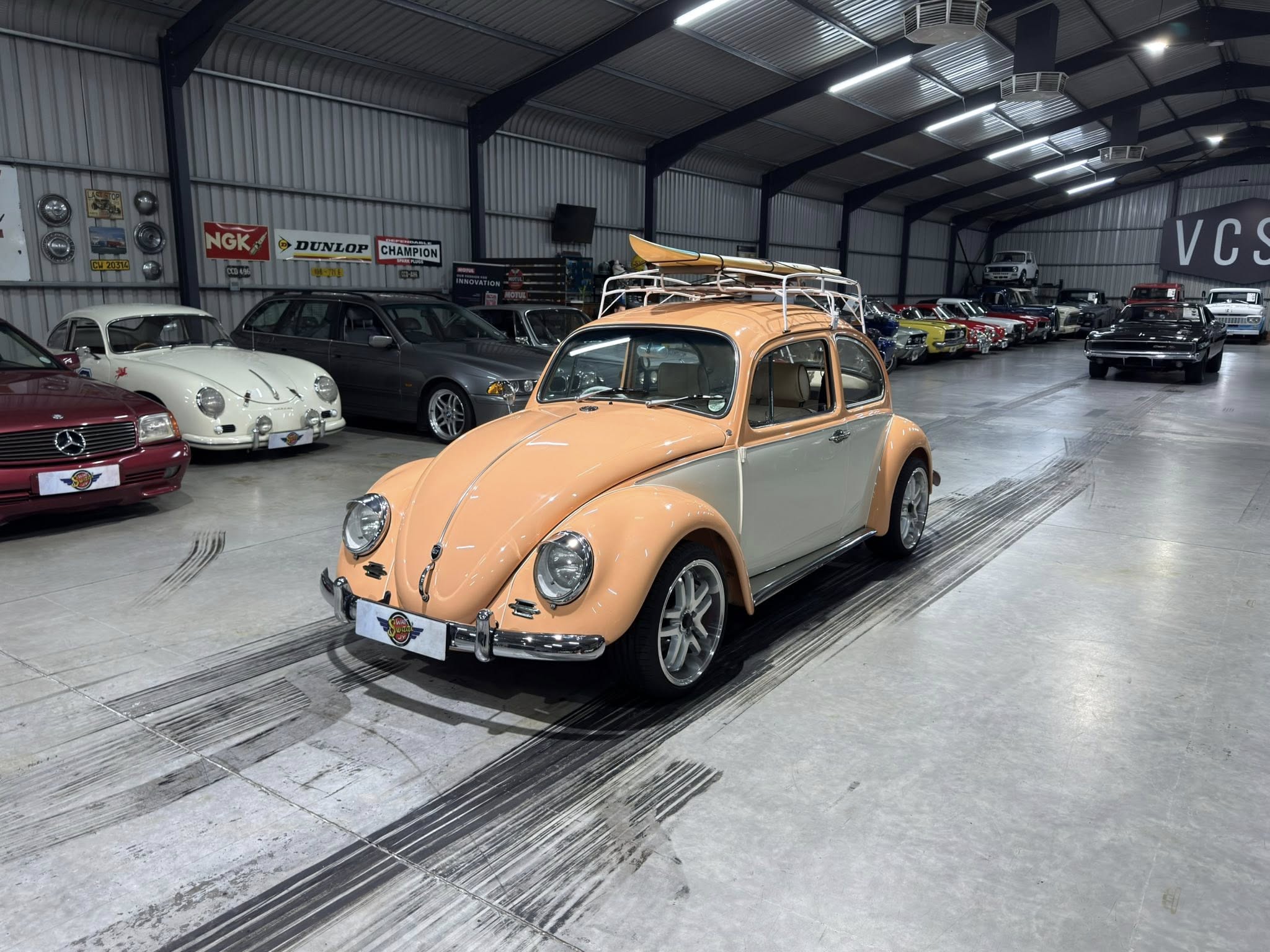 Interior of a car showroom filled with vintage vehicles, including an orange retro car with a roof rack and surfboard on top