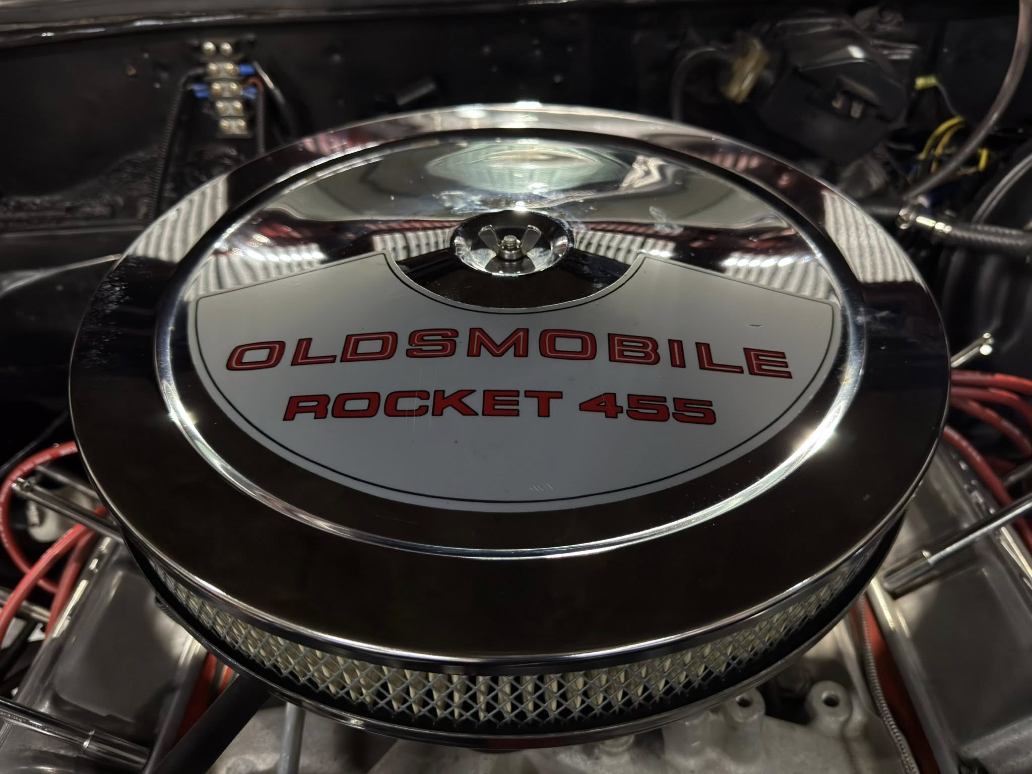 Close-up of a chrome engine air cleaner with 'OLDSMOBILE ROCKET 455' in red letters.
