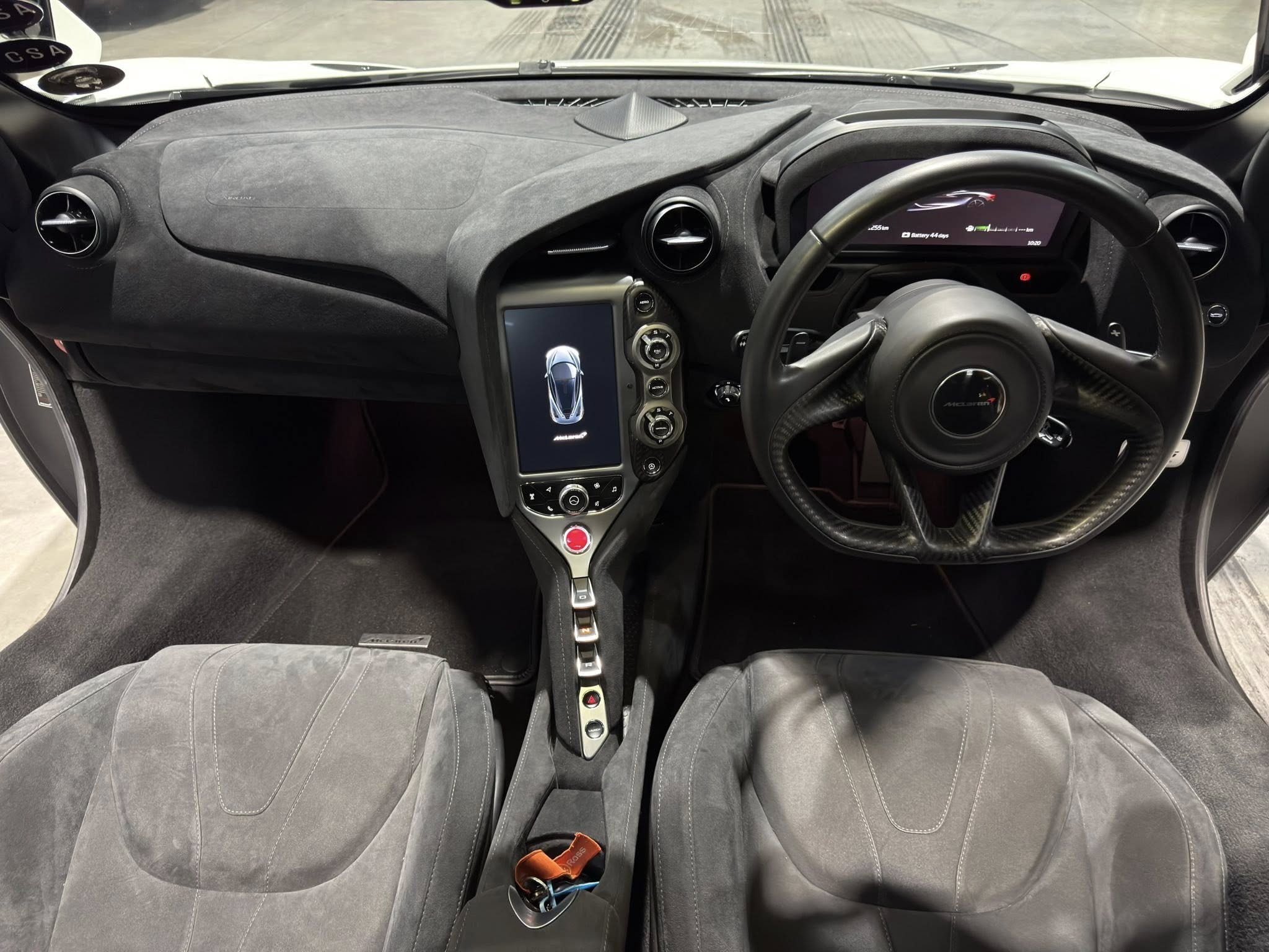 Right-hand-drive sports car cockpit with a suede-black dashboard, circular air vents, and a large digital display behind the steering wheel.