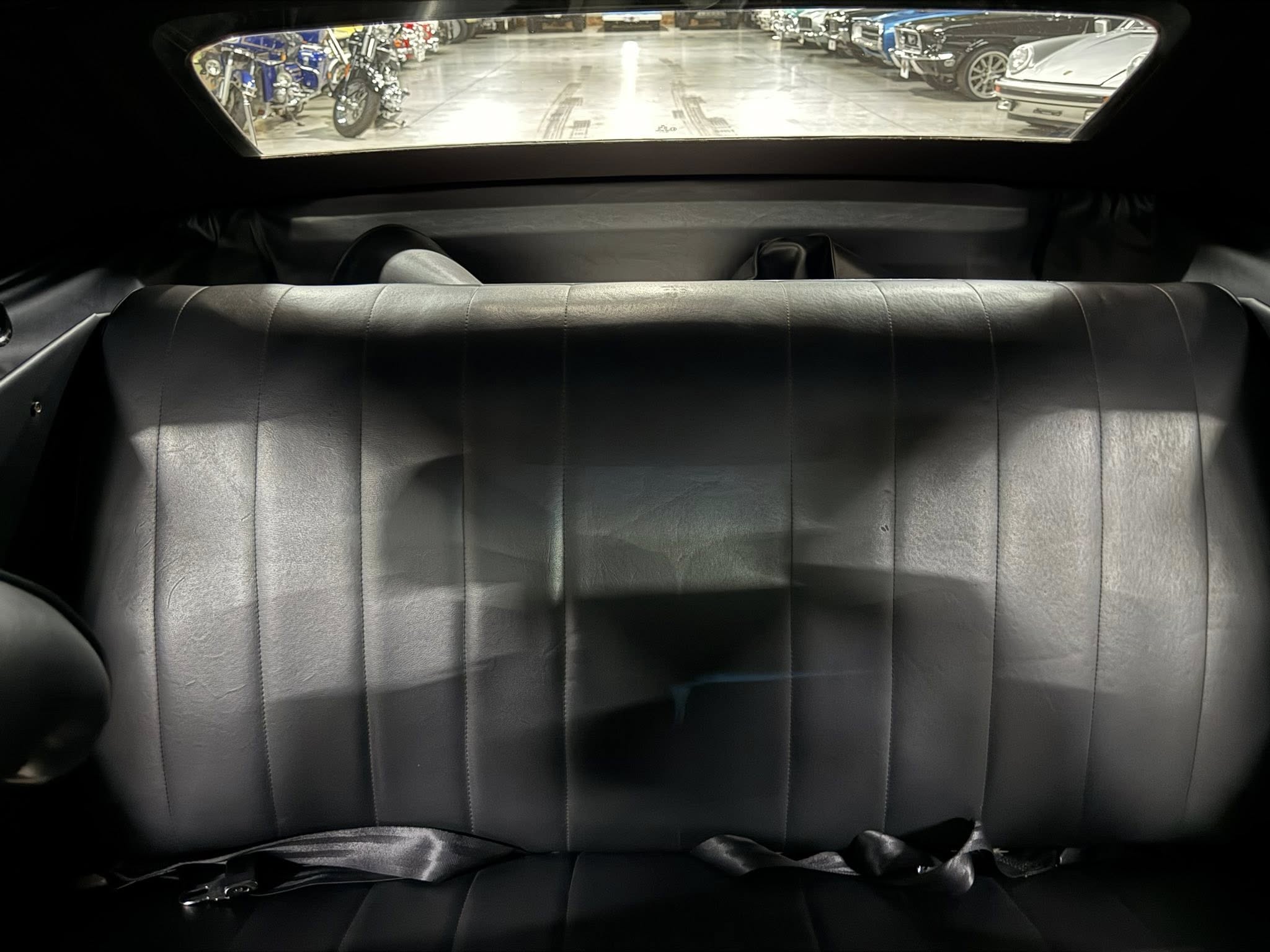 View from the back seat toward the rear window, showing an indoor parking area with motorcycles and classic cars lined up outside the glass.
